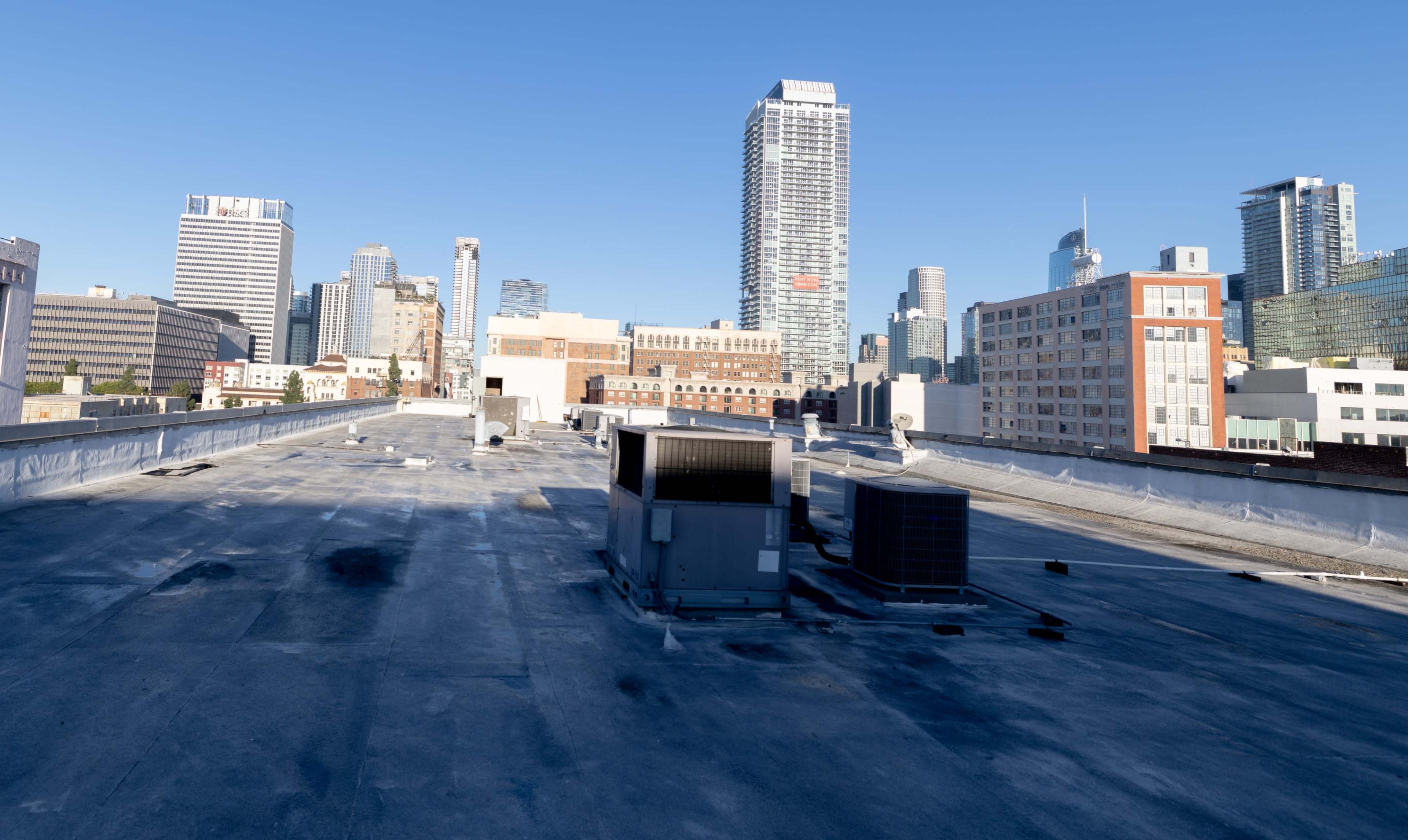 The image shows a rooftop view of a city skyline featuring various buildings and rooftop HVAC units under a clear blue sky.