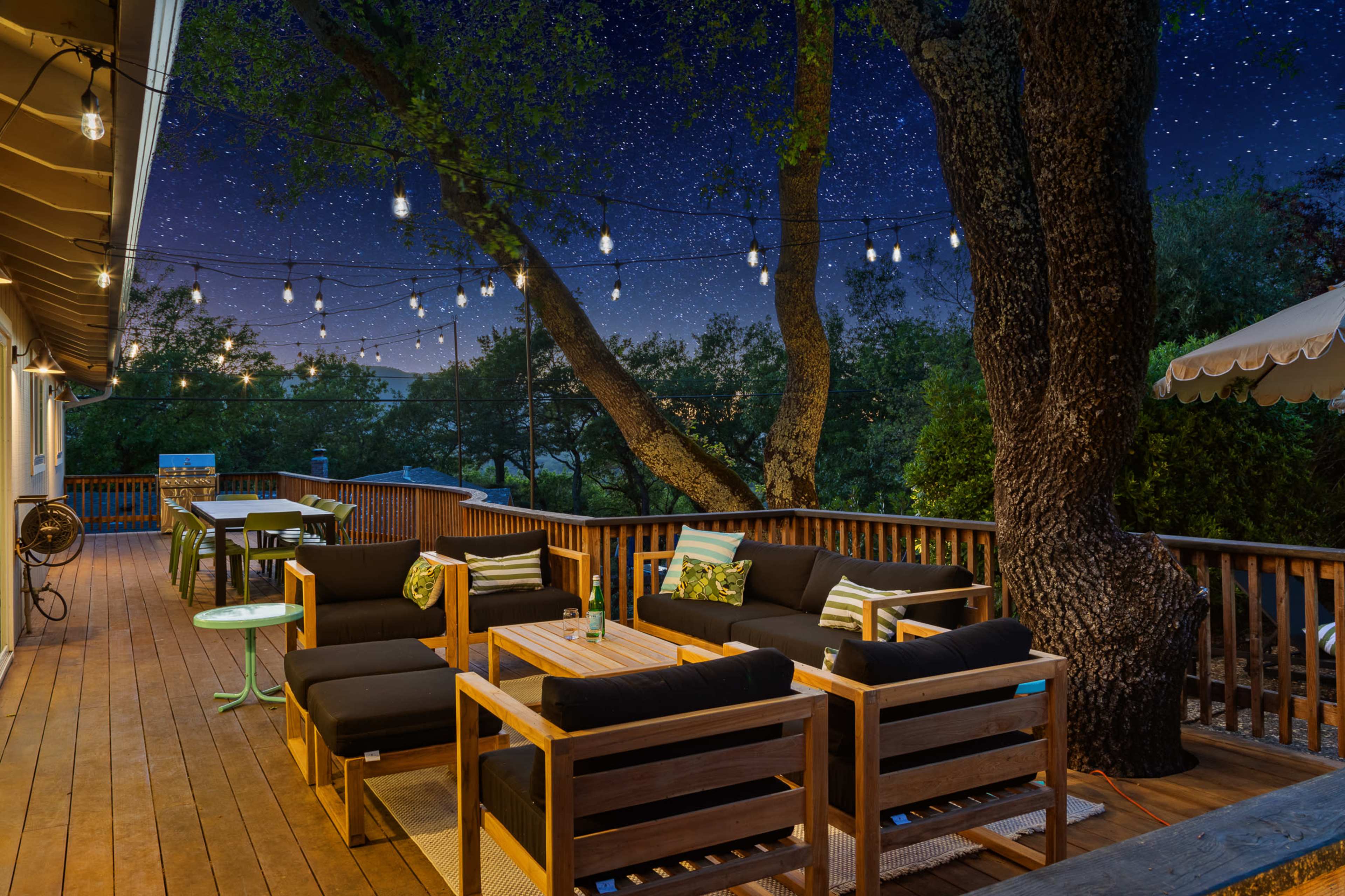 A cozy outdoor deck features wooden seating arrangements, a table, and string lights illuminating a starry night sky.