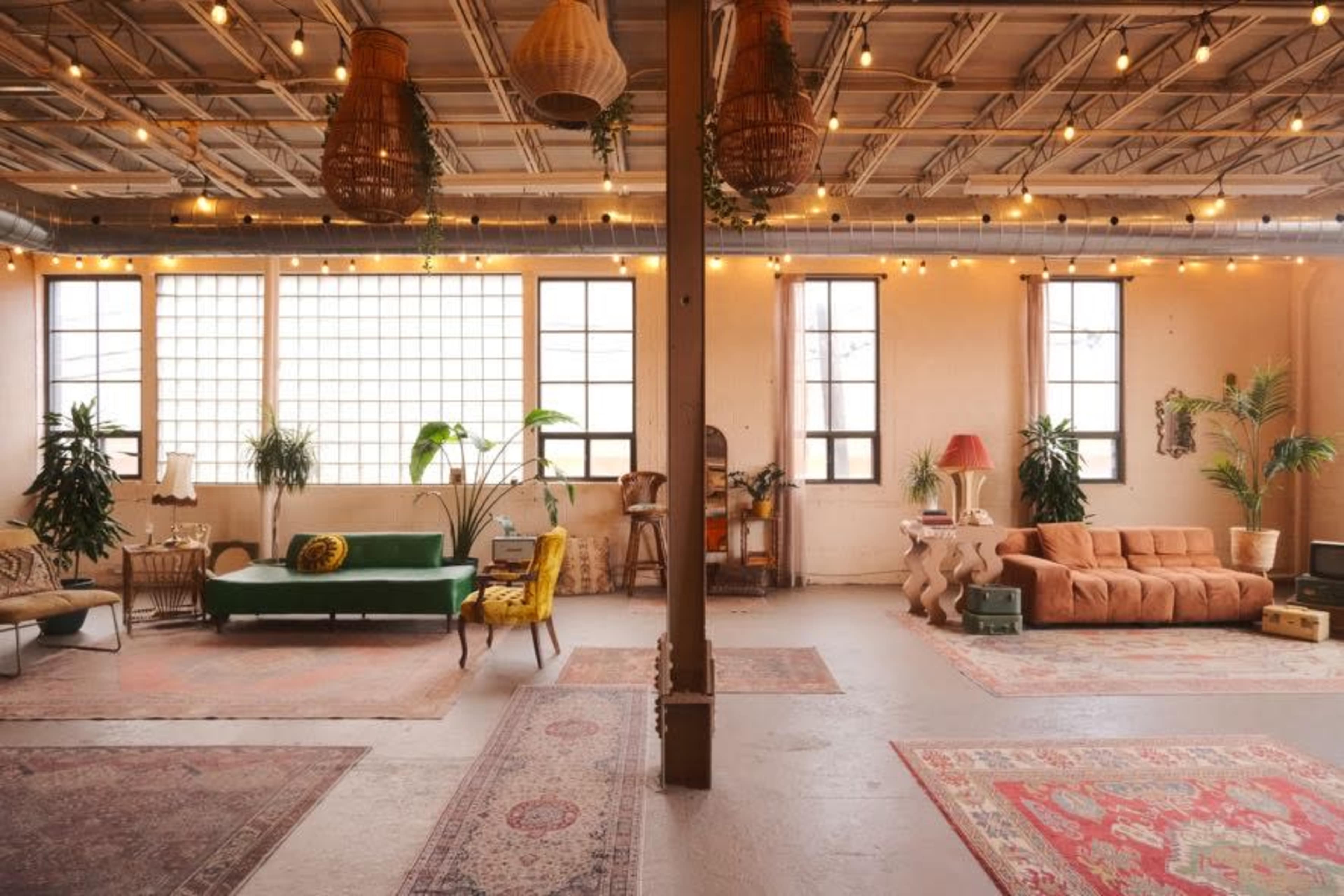 The image shows a spacious, brightly lit loft adorned with various seating options, plants, and decorative rugs.