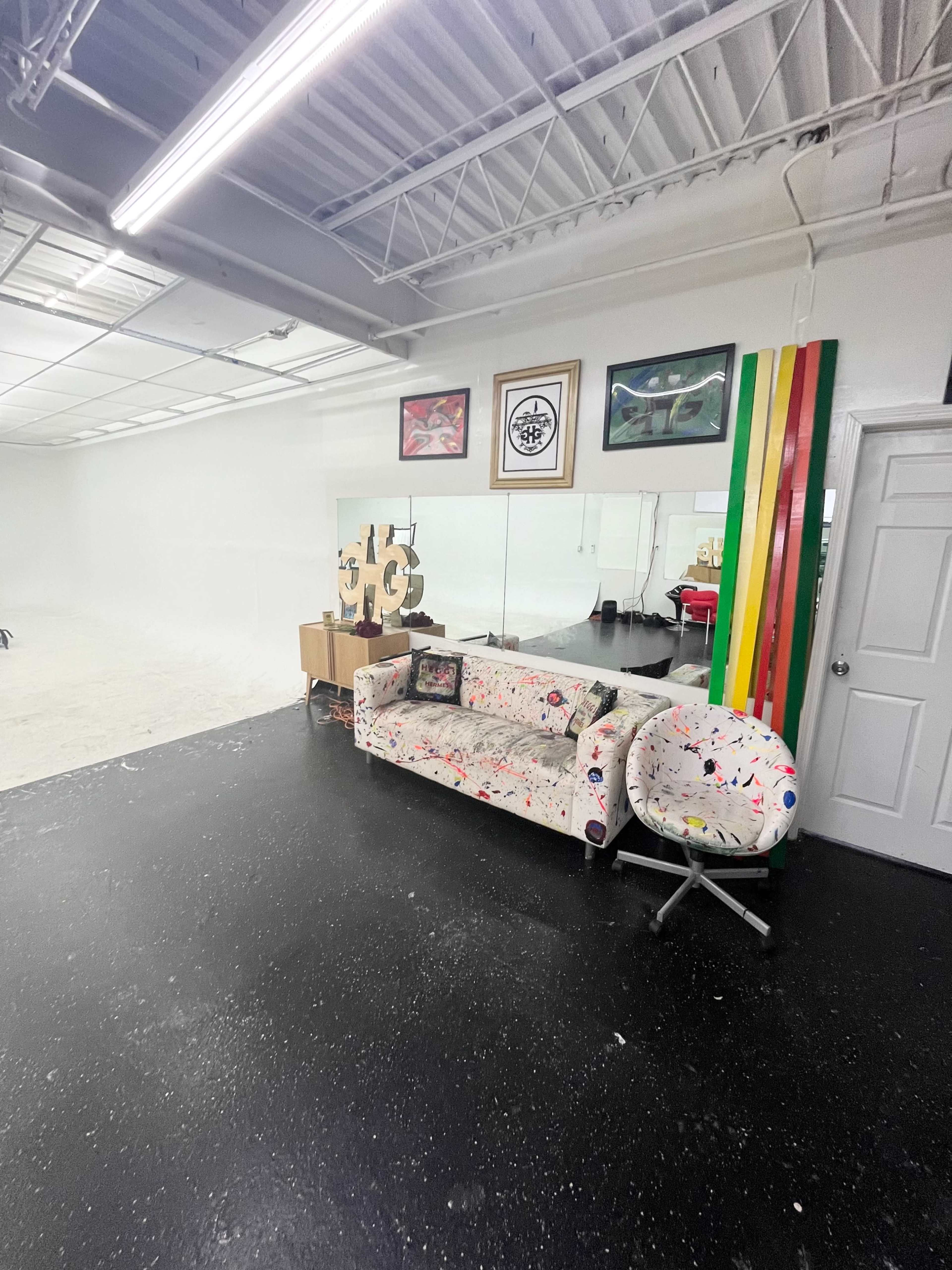 The image shows a spacious room with a patterned sofa, a round chair, and various framed artworks on the walls.