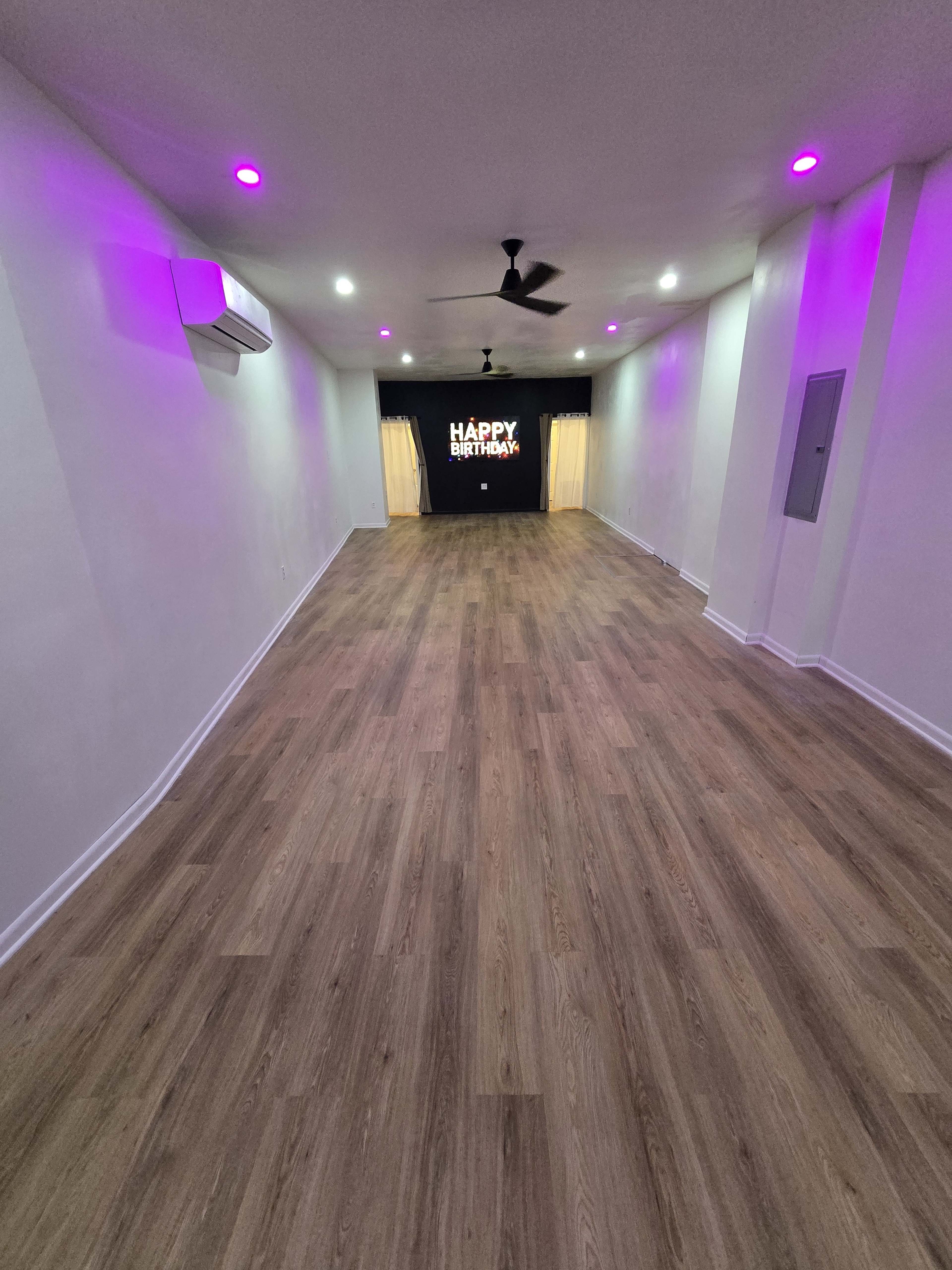 The image shows an empty venue with wooden flooring, pink lighting, and a backdrop displaying "Happy Birthday."
