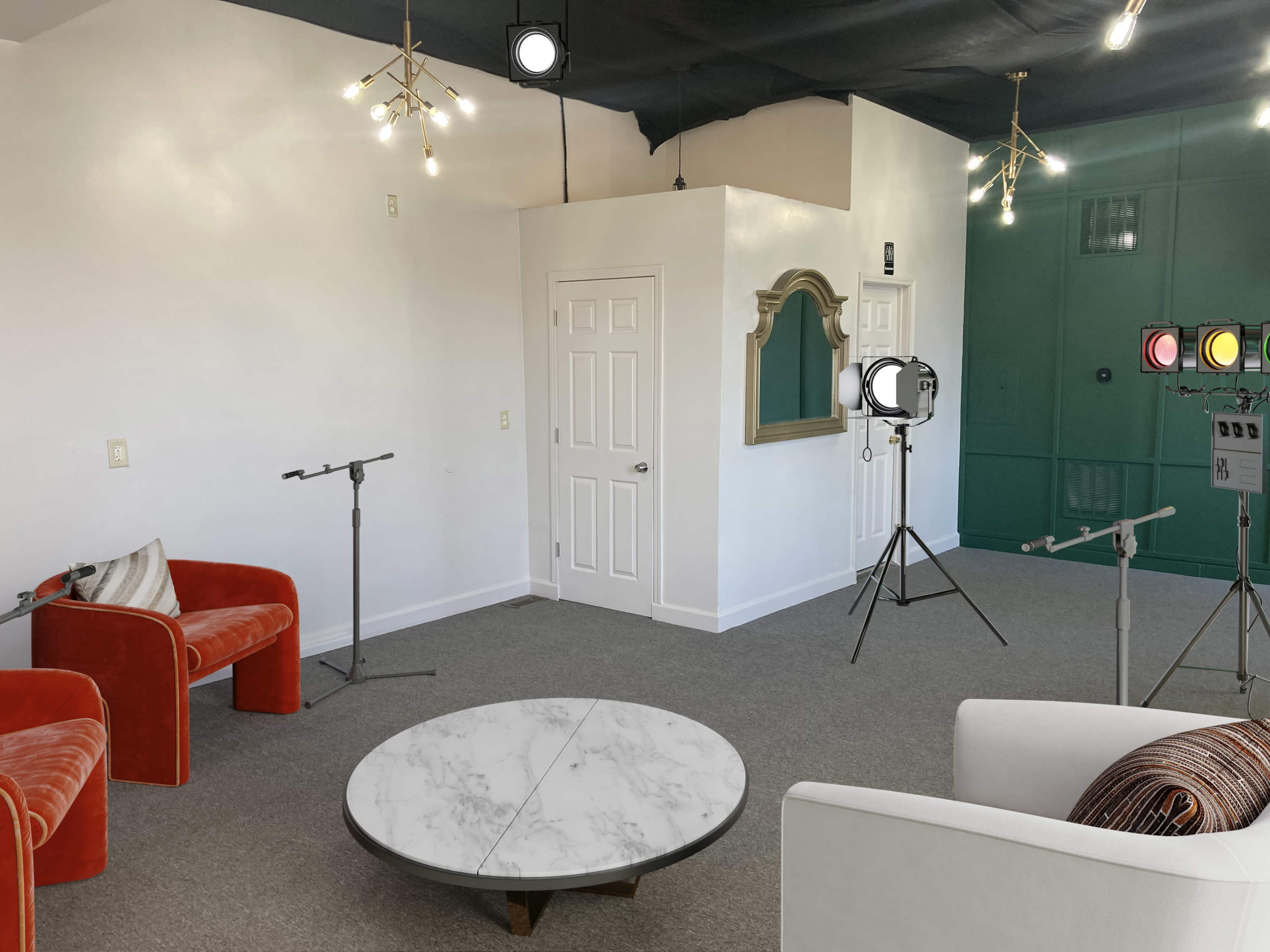 The room features a seating area with two red chairs and a white couch, a round marble coffee table, and studio lighting equipment set up in a spacious, empty environment.