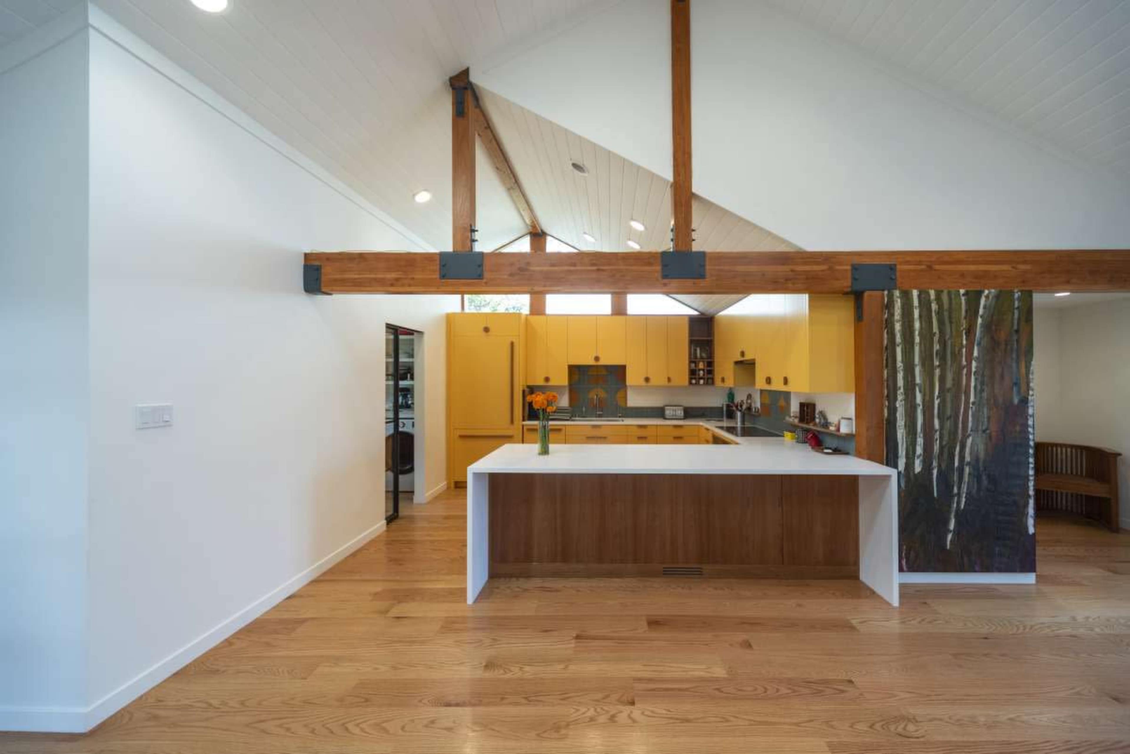 The image shows a modern kitchen with a central island, wooden beams, and yellow walls.