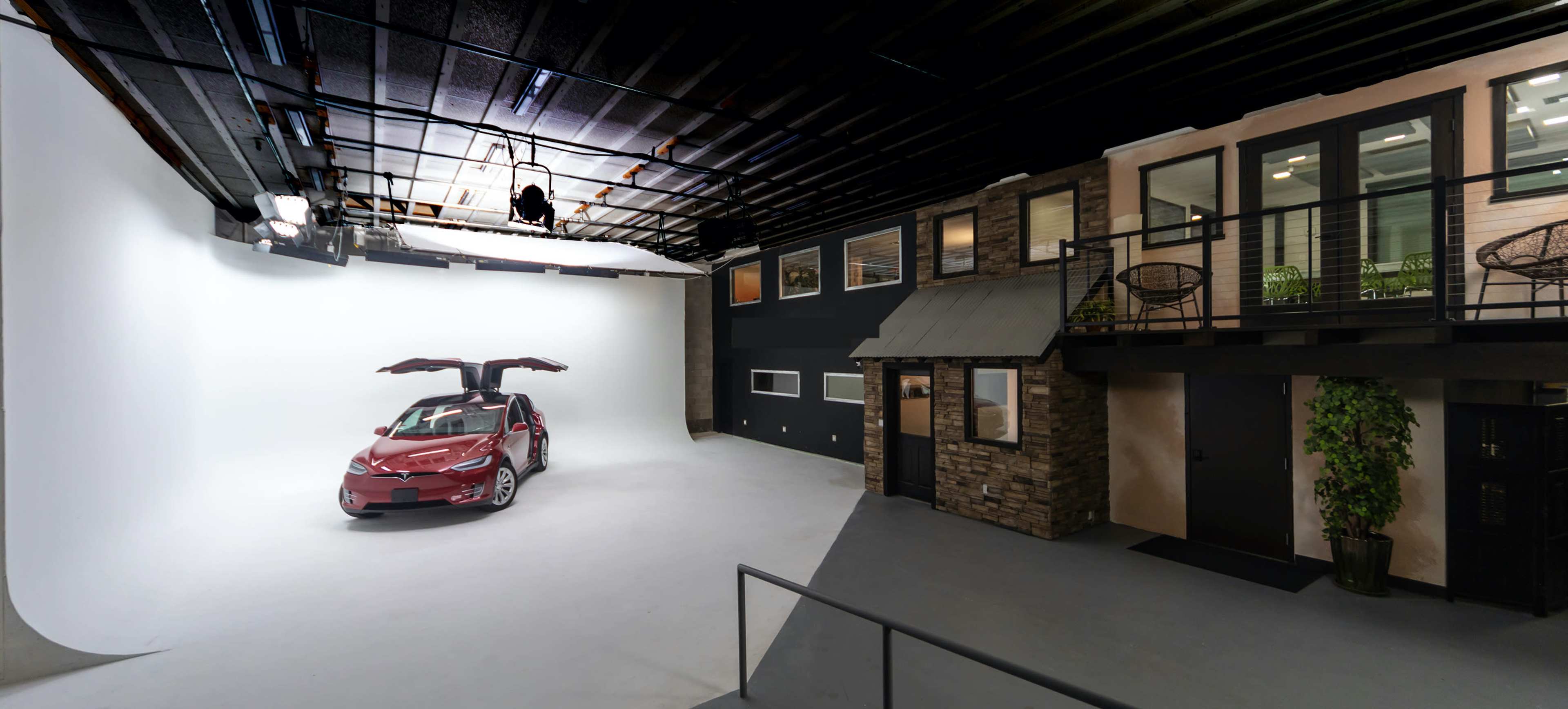 A spacious photo studio with a red car in the center and a two-story structure resembling a house on the right side.
