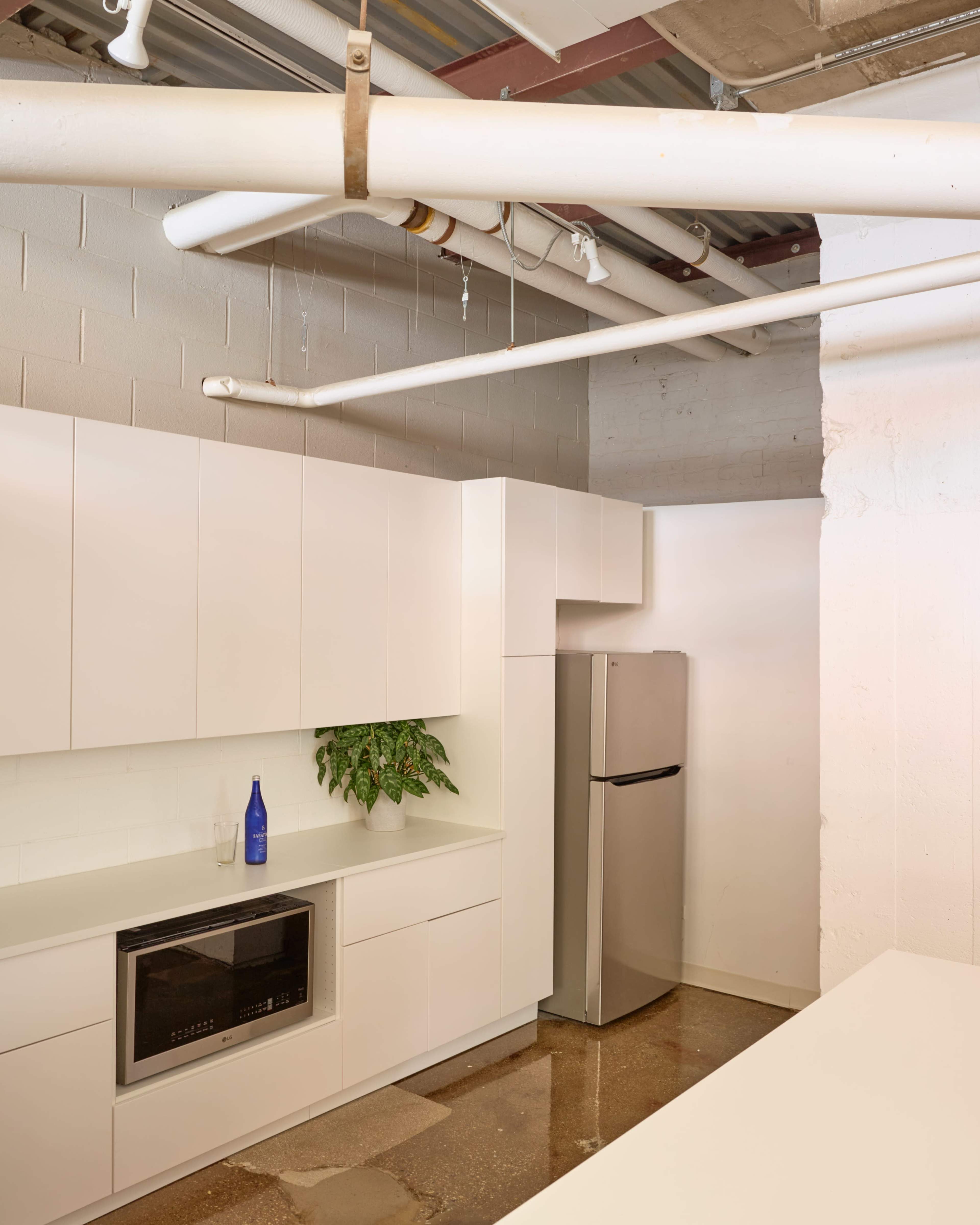 A modern kitchen features white cabinetry, a stainless steel refrigerator, and a countertop with a small potted plant.