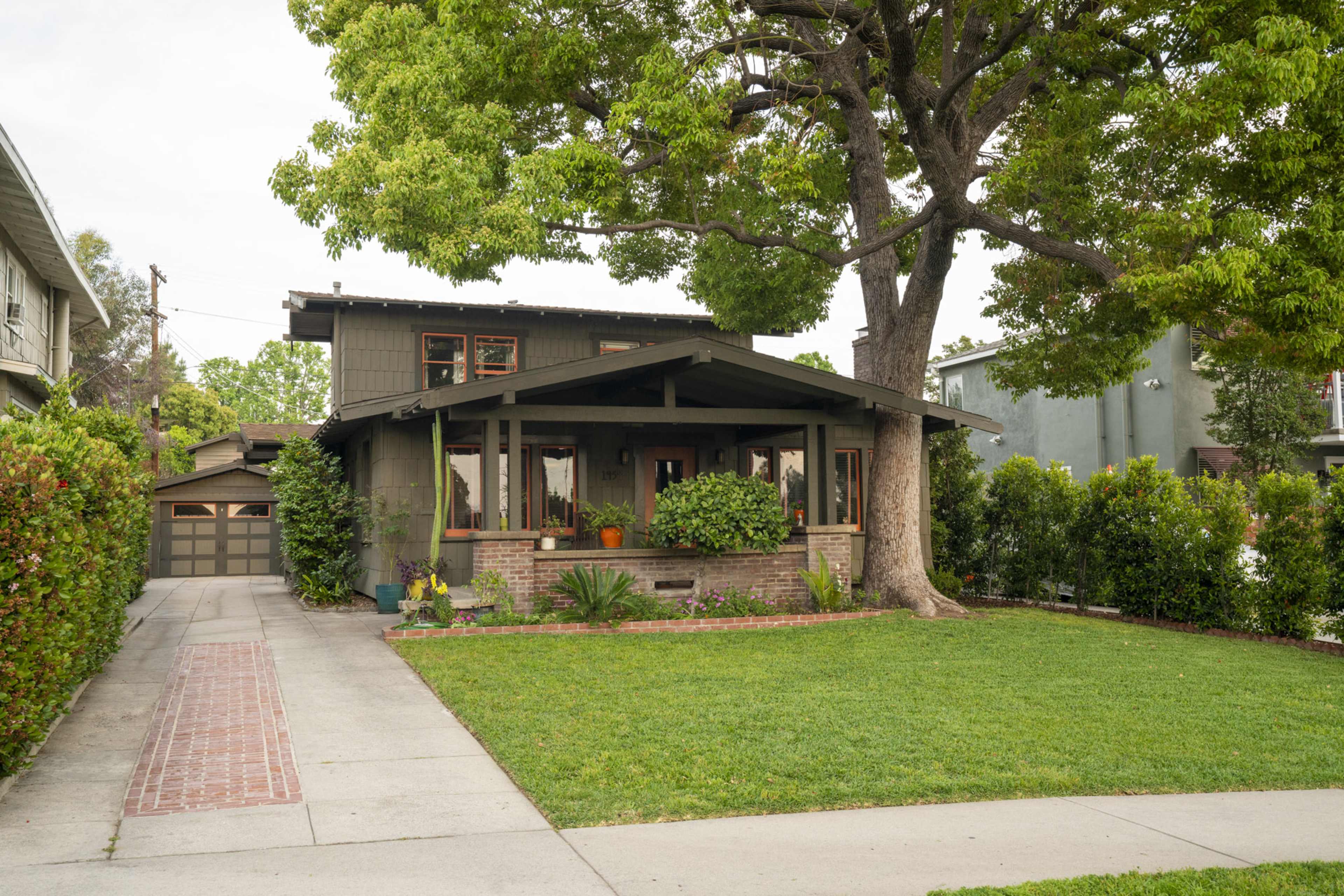 A two-story house with a front porch, surrounded by grass and trees, sits at the end of a paved driveway.