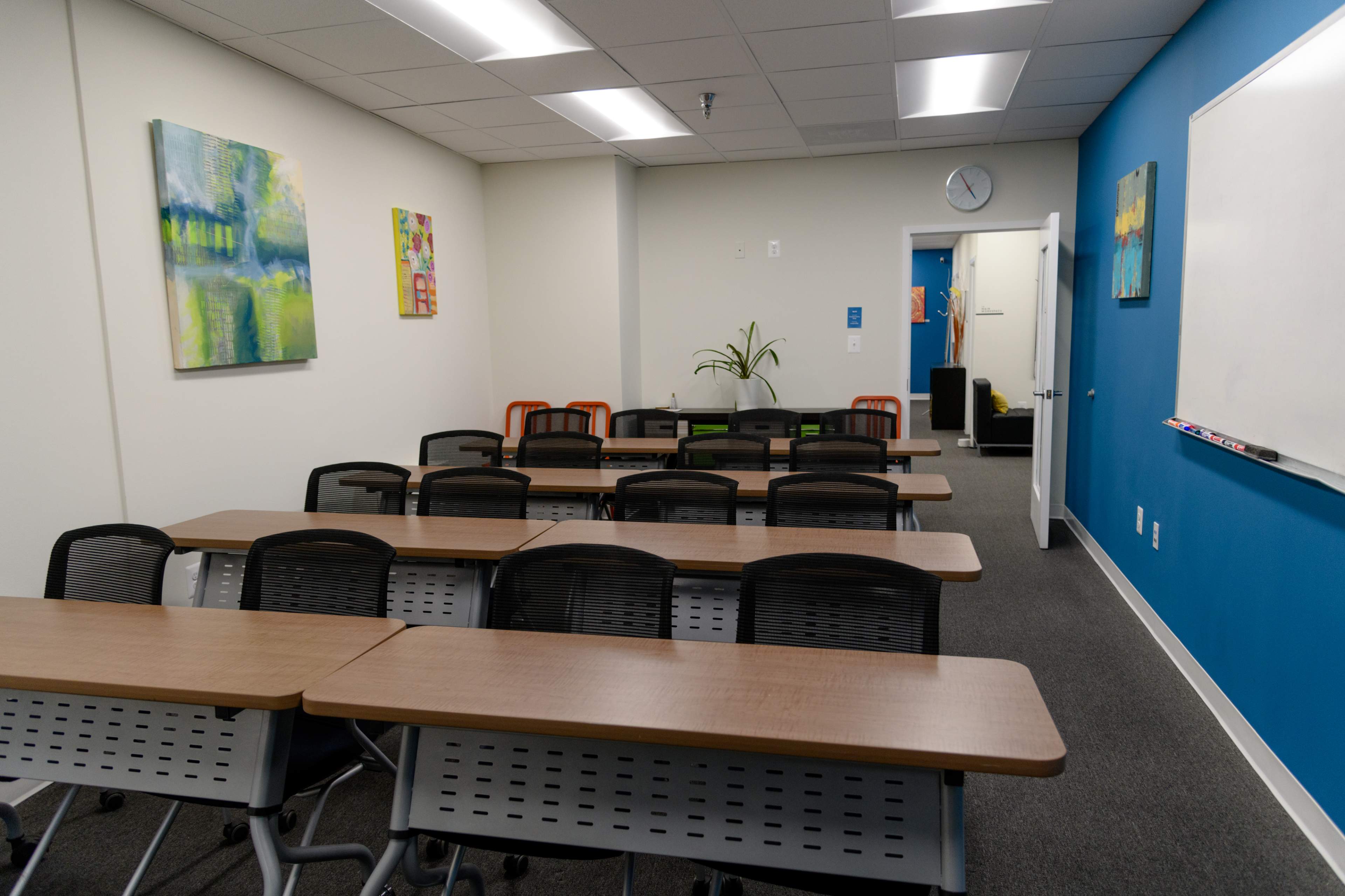 A classroom equipped with several rows of tables and chairs, colorful artwork on the walls, and a whiteboard.
