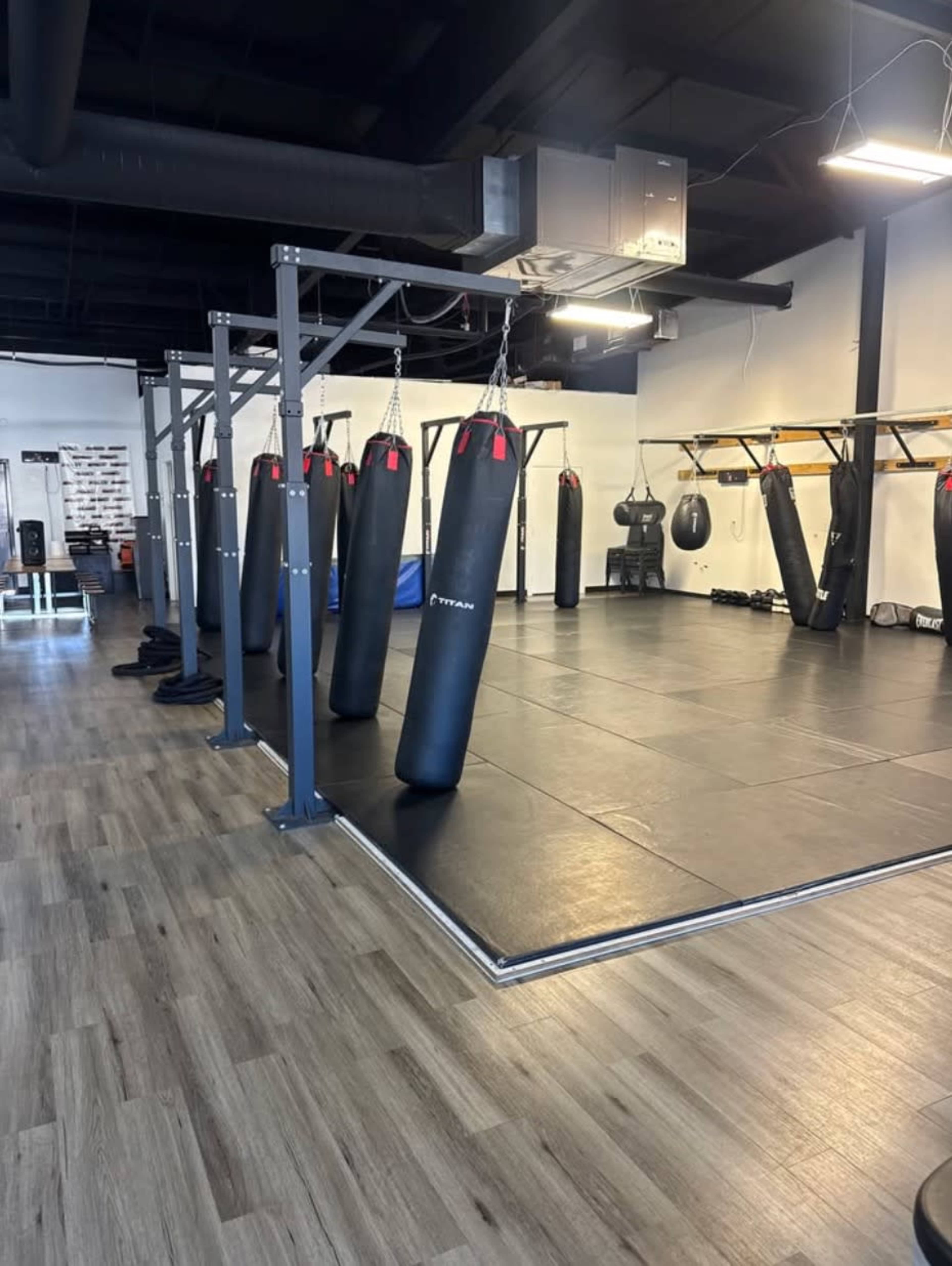 The image shows an empty boxing gym with several heavy punching bags hanging from a metal frame.
