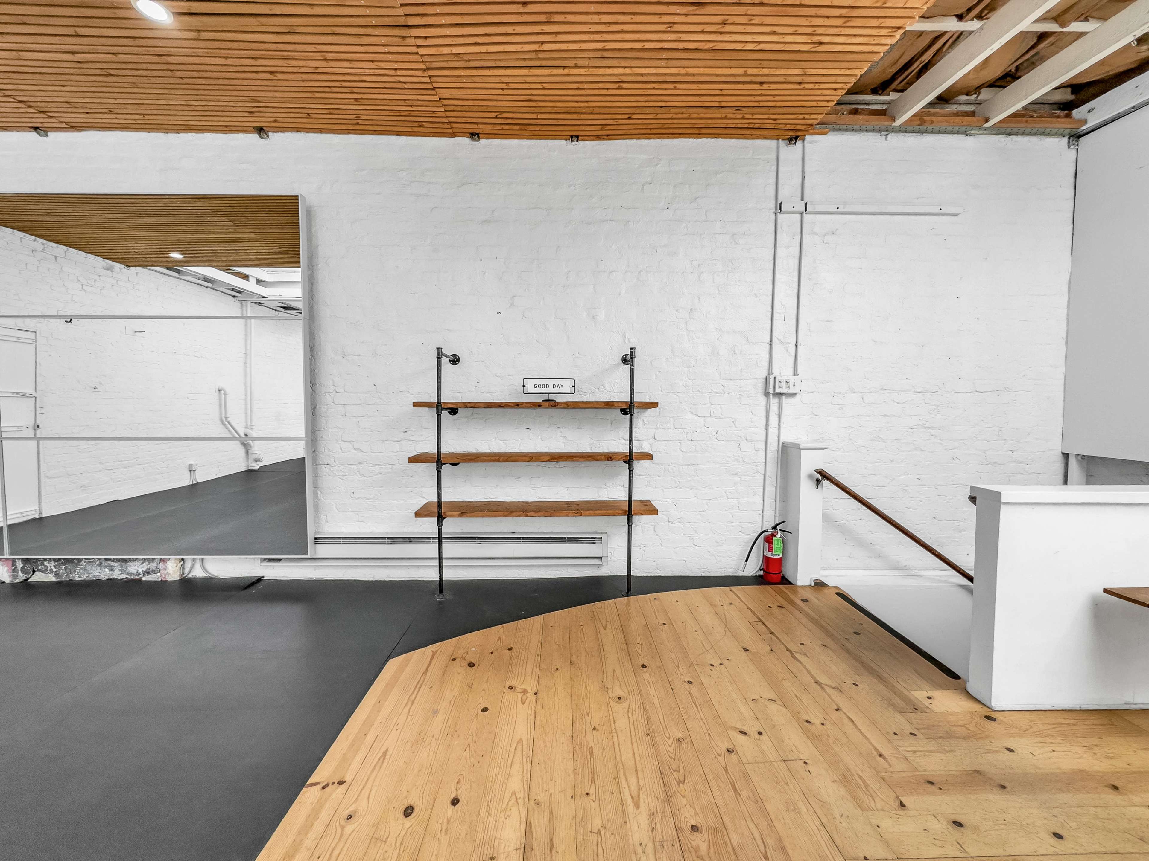 A spacious, well-lit interior of a room with wooden shelves, a large mirror, and a black rubber floor.