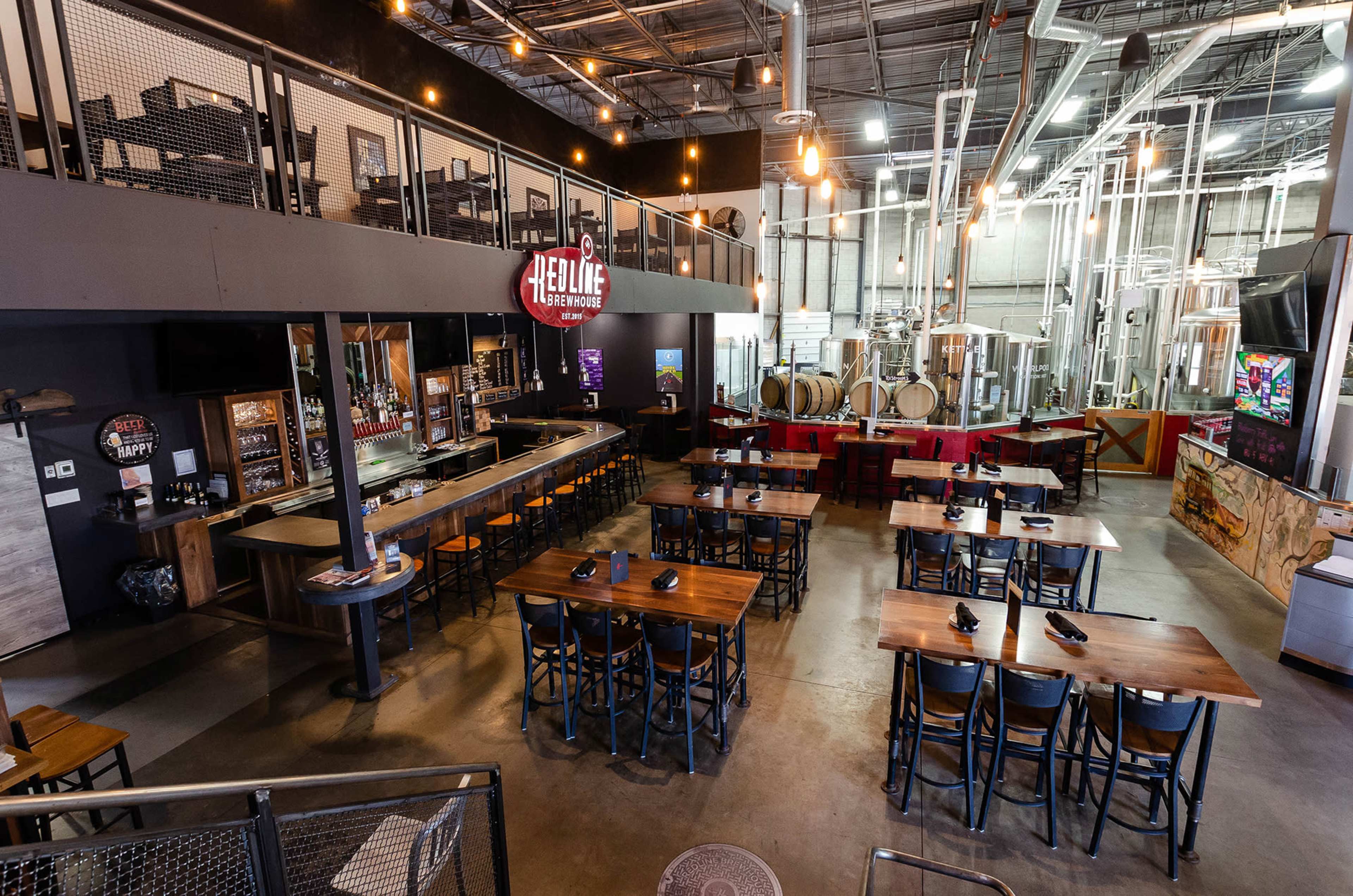 An interior view of a restaurant with a bar area, dining tables arranged in rows, and visible brewing equipment in the background.