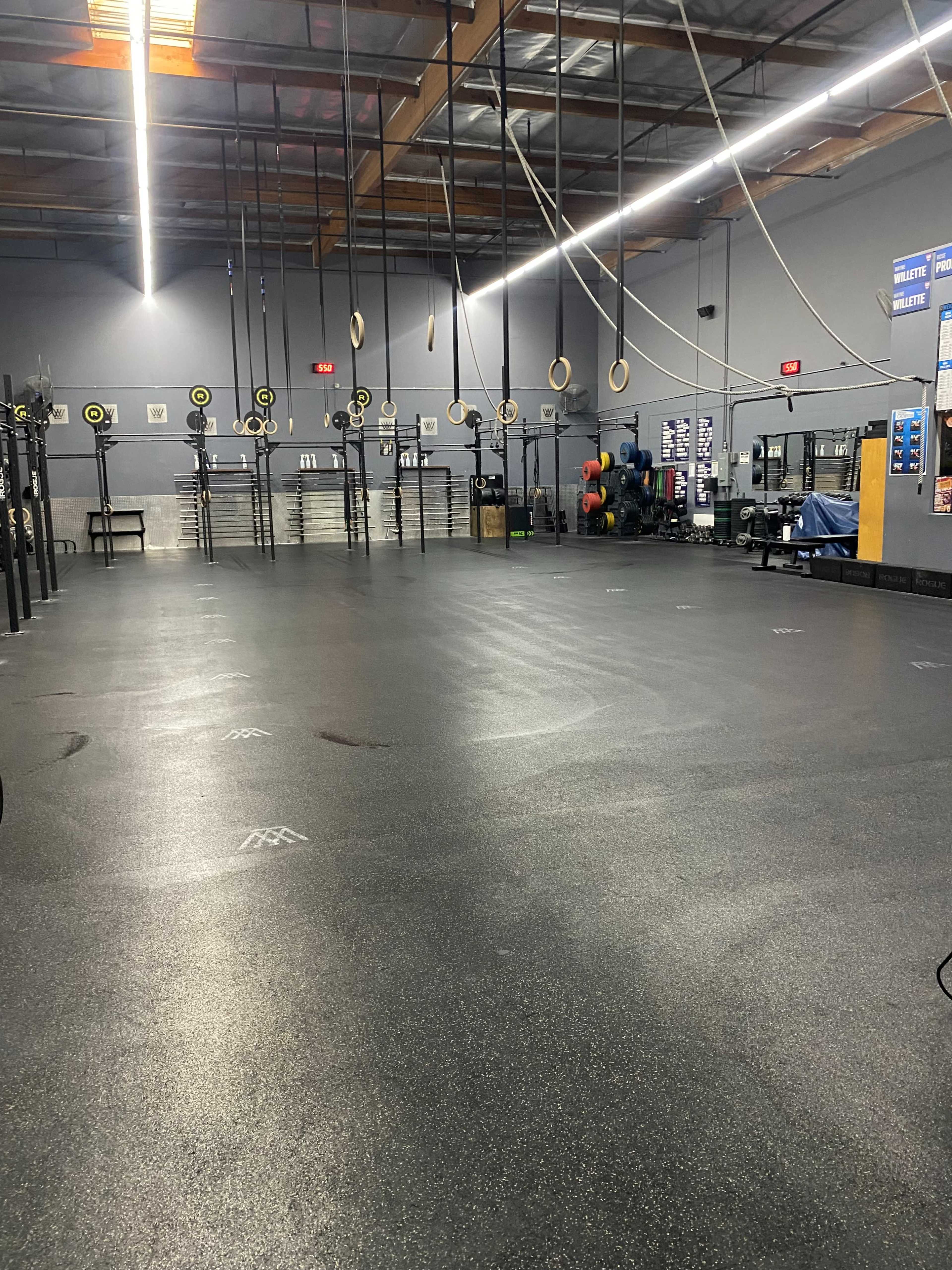 An empty gym with various exercise equipment, black flooring, and suspended ropes and rings from the ceiling.