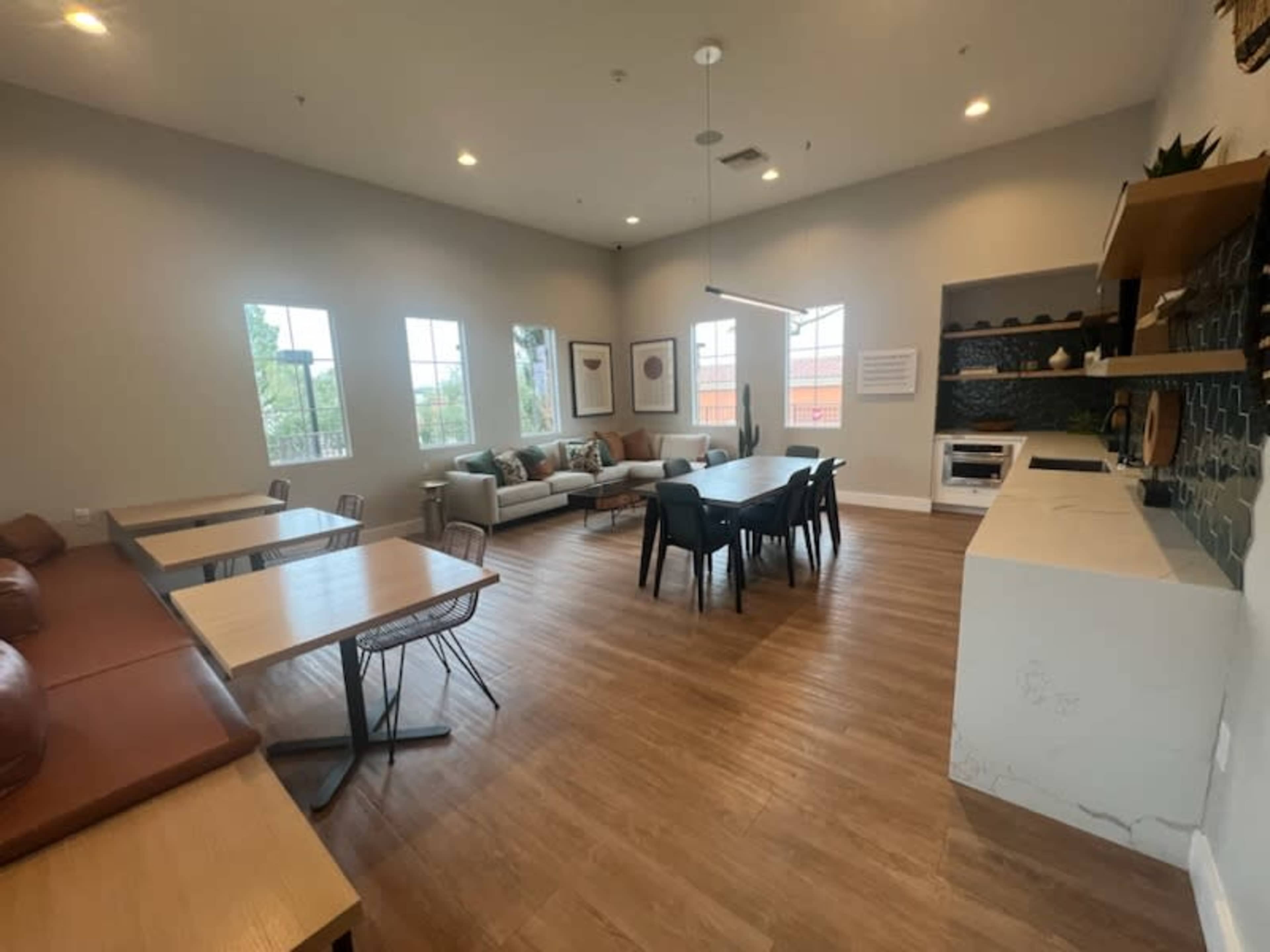 A modern communal space featuring a seating area with a sofa, tables, and a kitchenette with decorative elements.