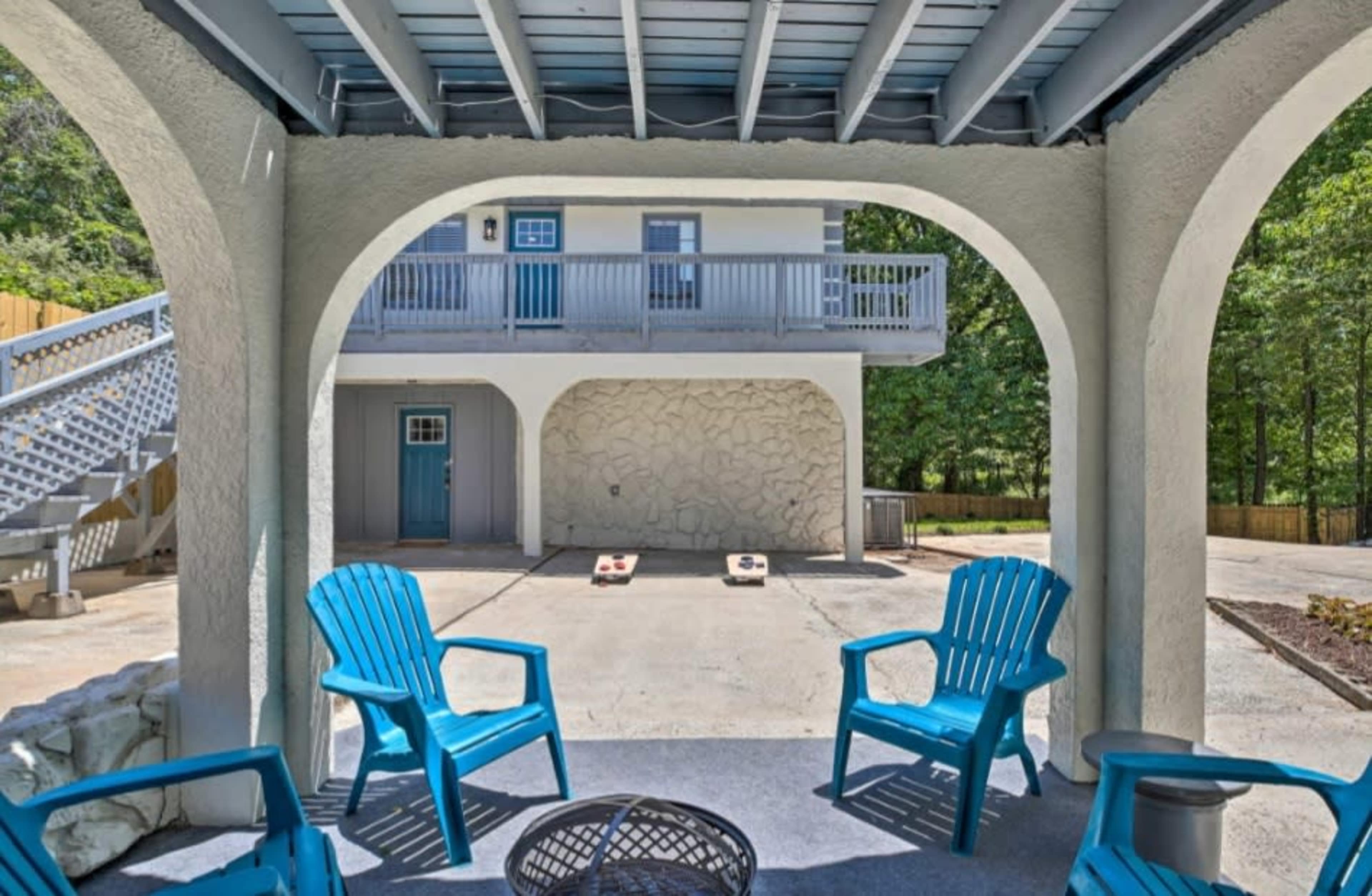 The image shows a covered patio with four blue chairs facing a concrete area, with a house and steps visible in the background.