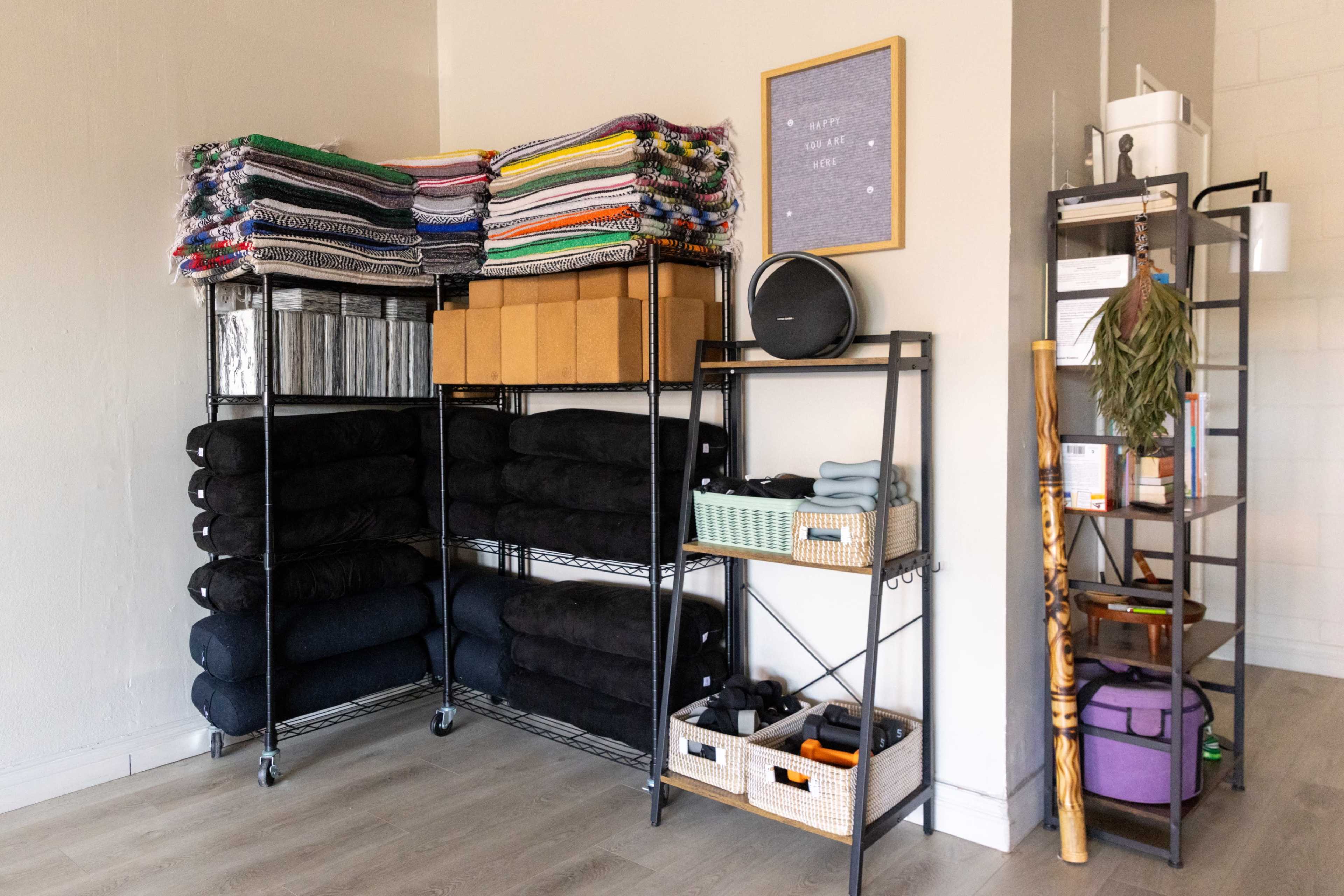 The image shows a neatly organized room featuring shelves stacked with colorful blankets, black towels, storage boxes, and various items on a metal shelving unit.