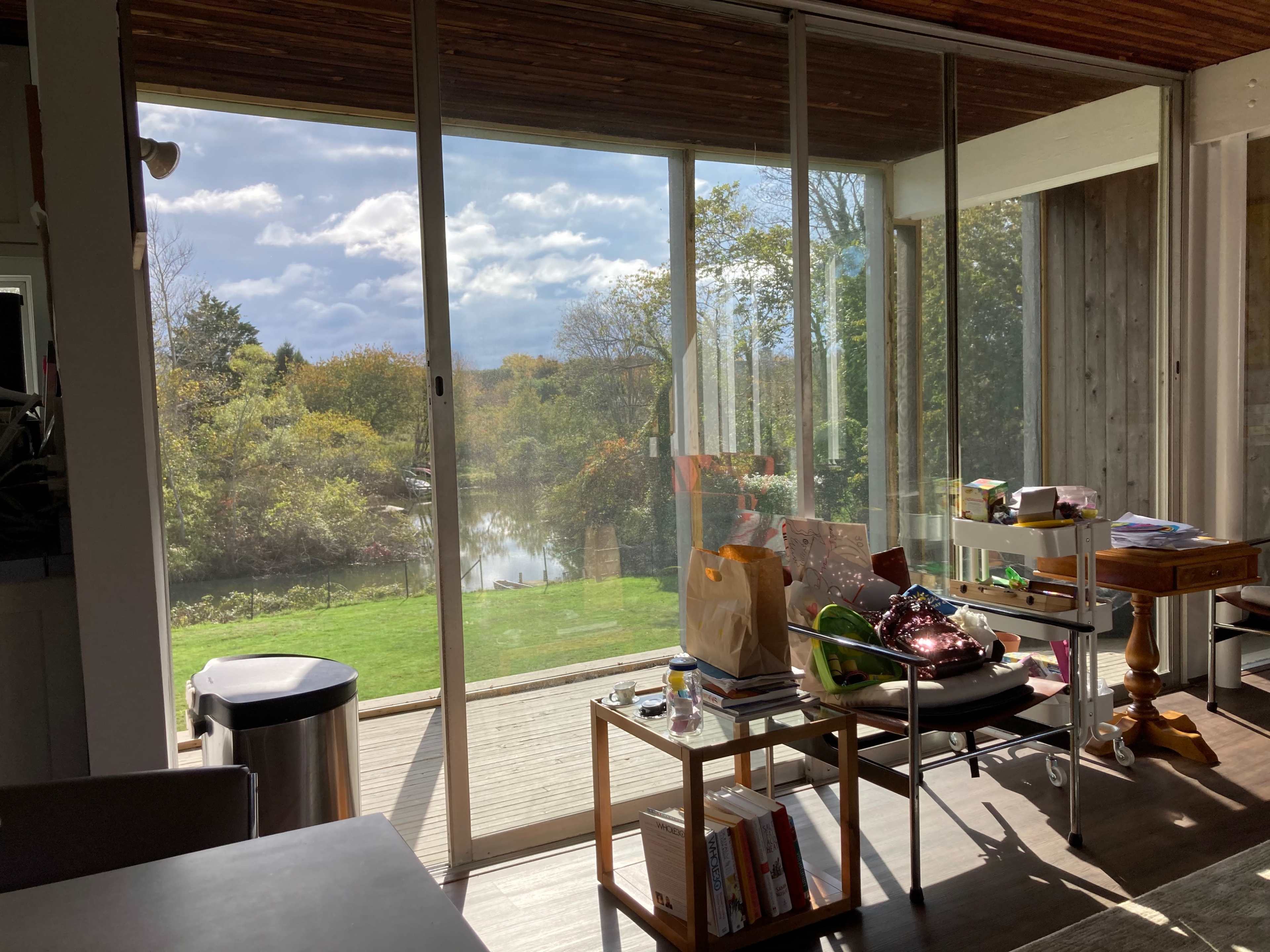 A glass sliding door opens to a view of a serene landscape with trees and a body of water.
