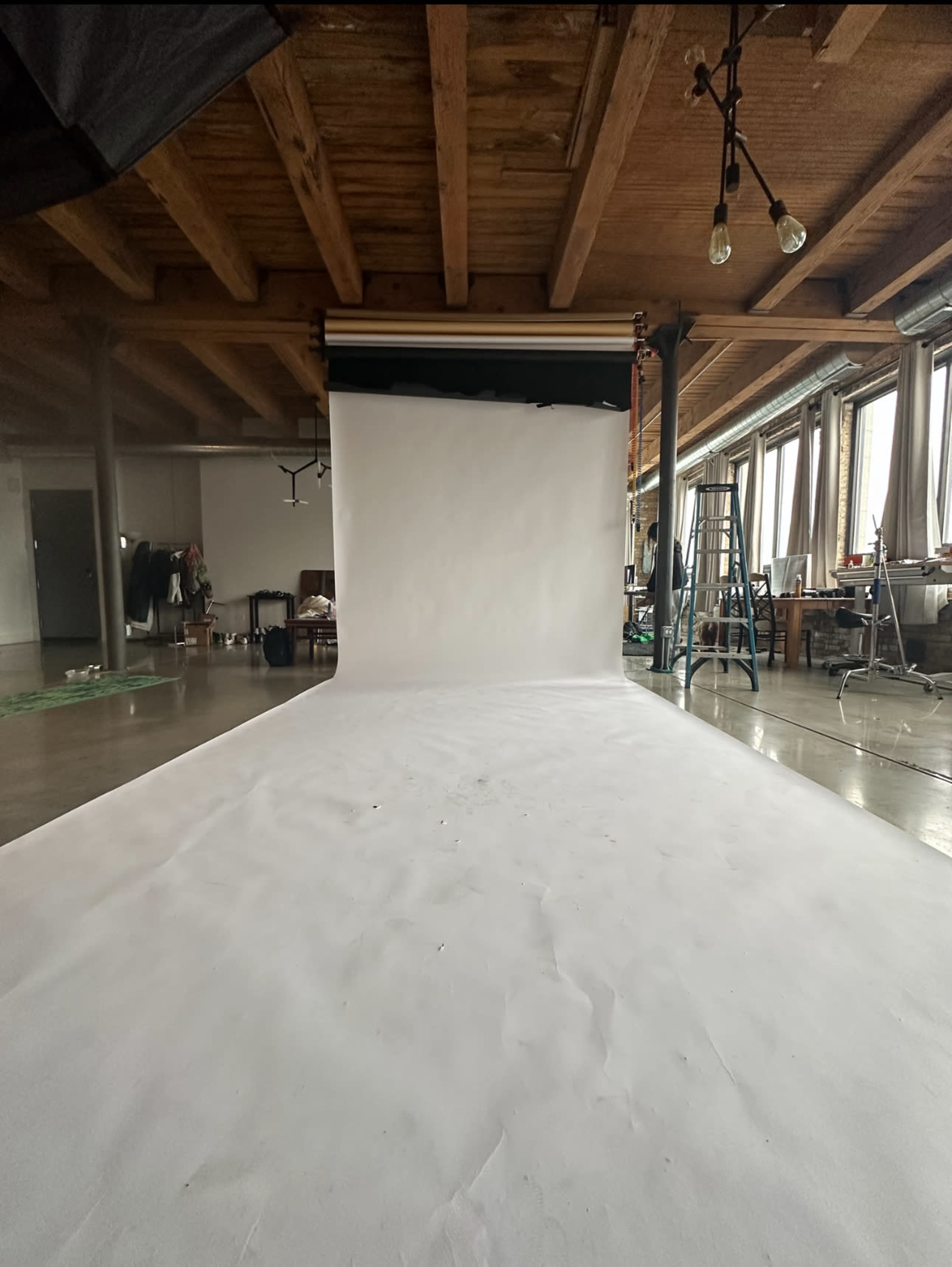 A photography studio featuring a seamless white backdrop, a ladder, and various furniture in a spacious, well-lit environment.