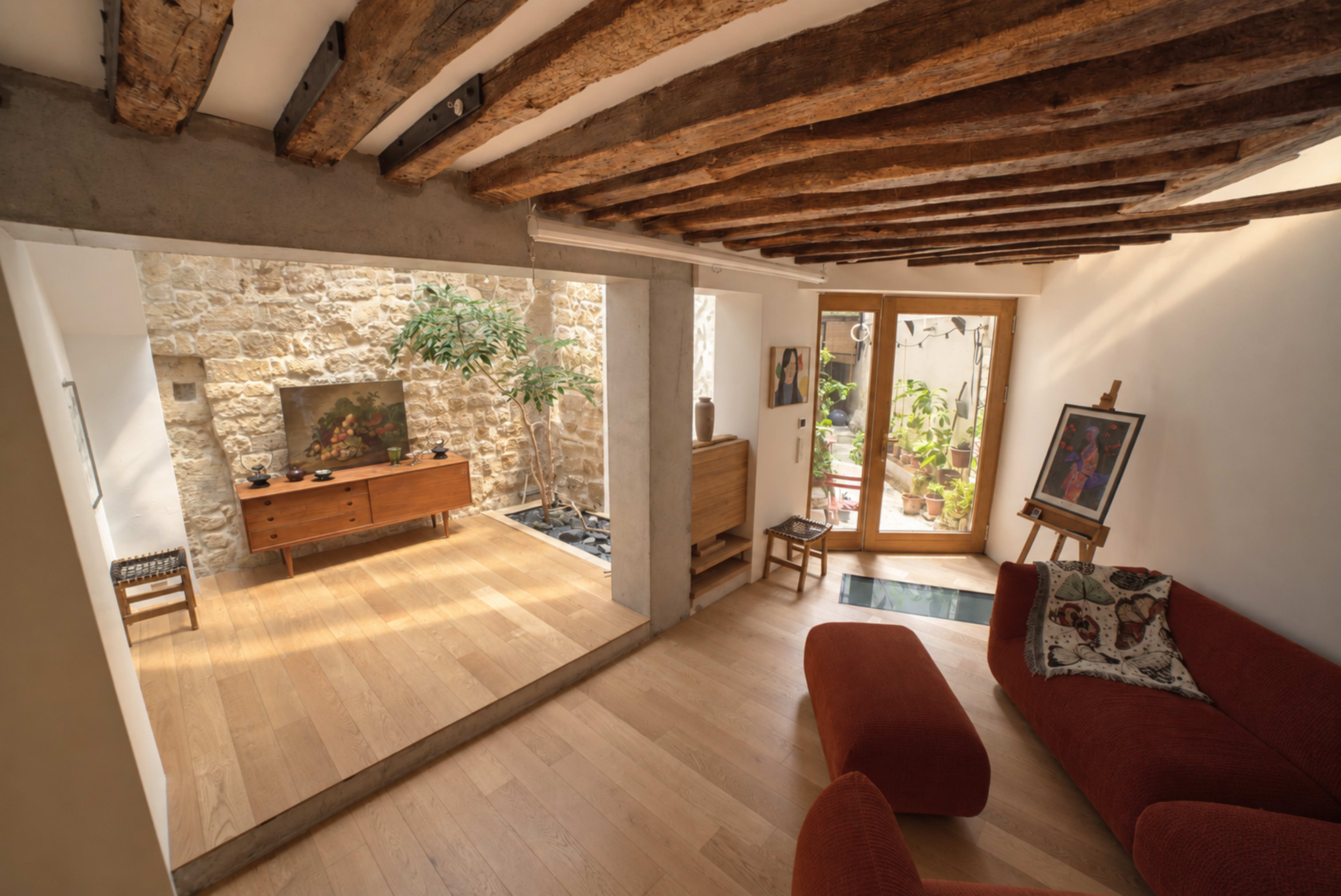 A spacious living area features a wooden floor, exposed beams, and a light-filled corner with plants and a fish tank.