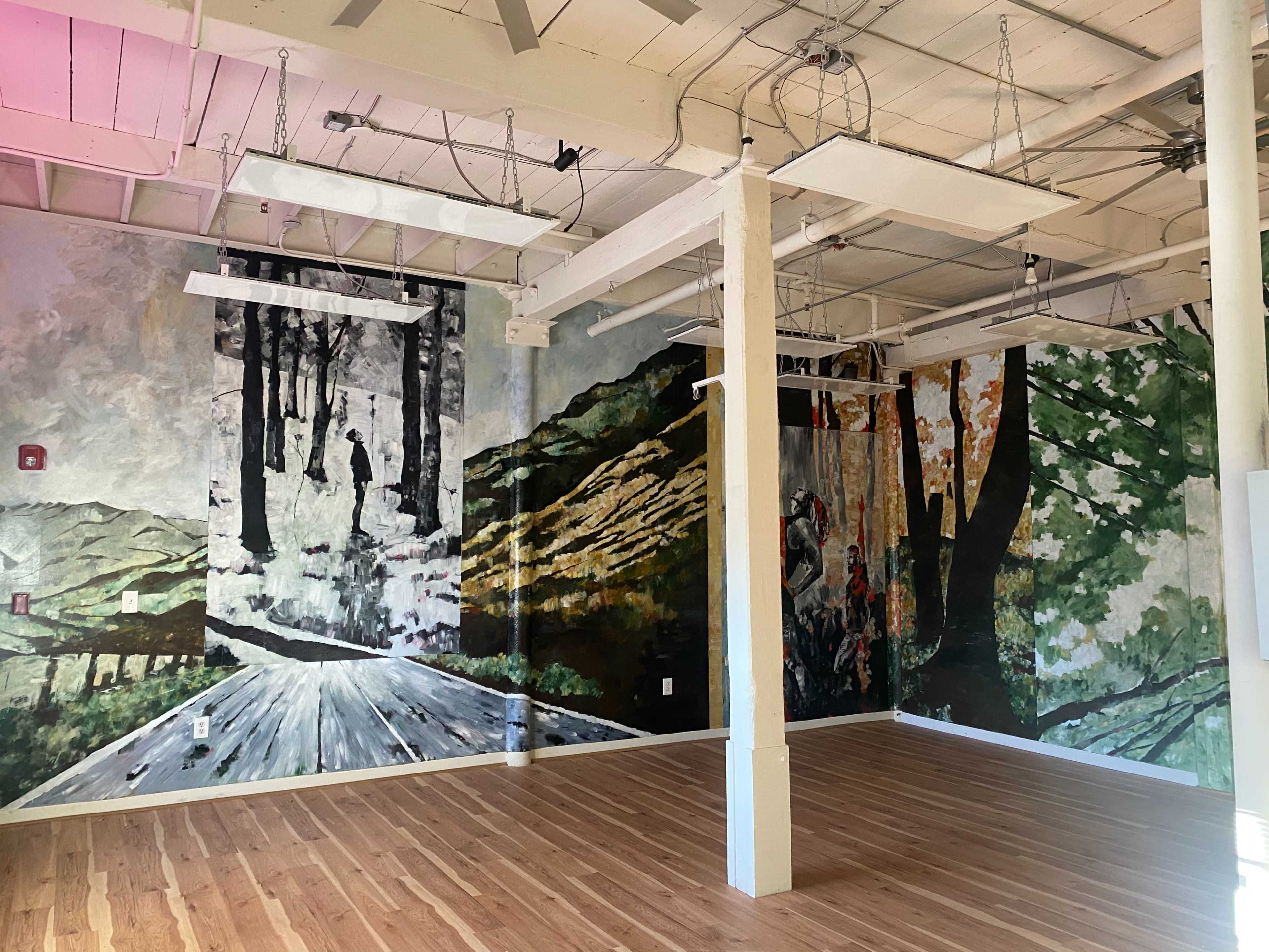 A spacious room with wood flooring and large murals depicting forested landscapes on the walls.