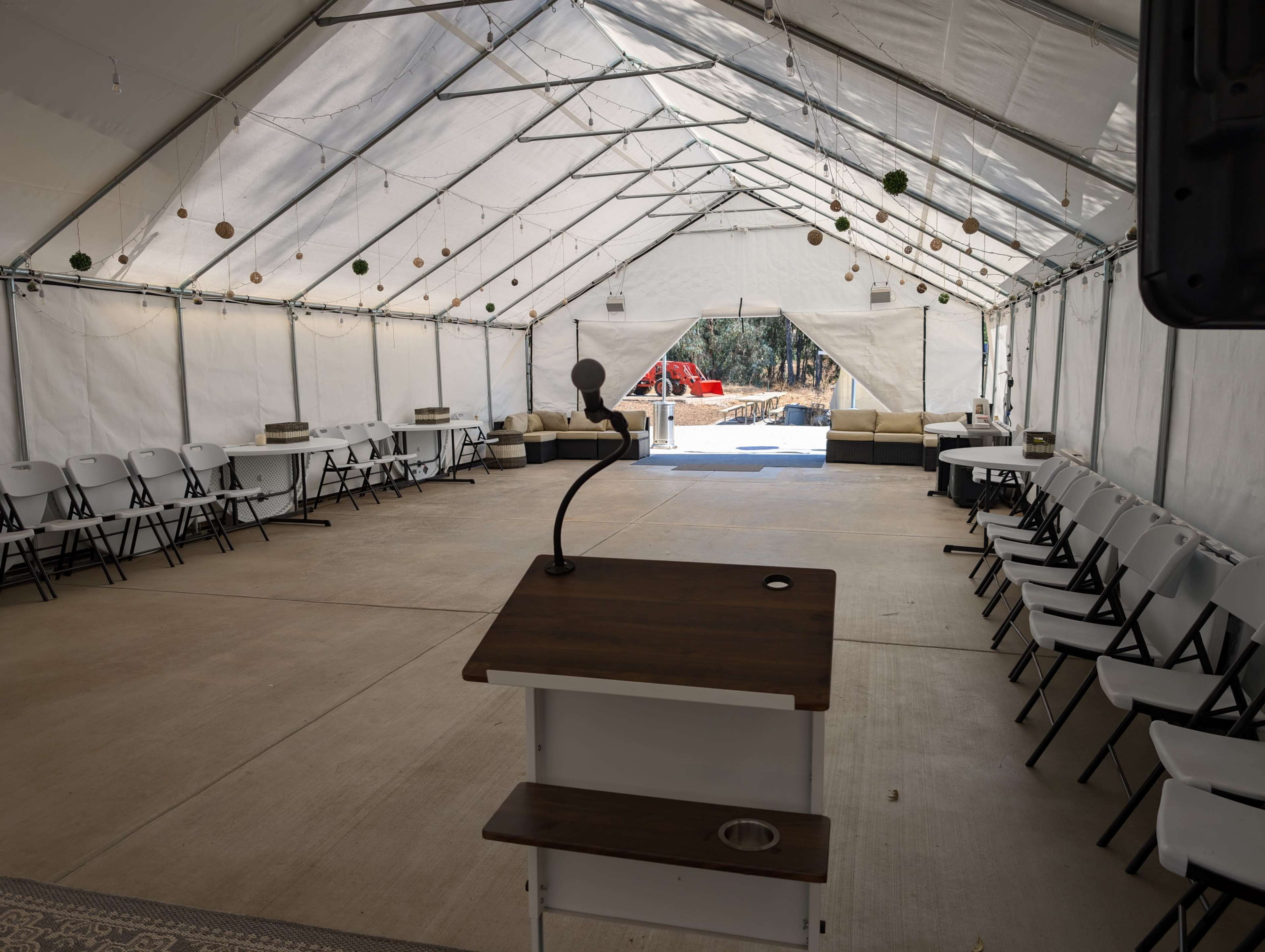 The image shows an empty tent with white folding chairs arranged around tables, and a podium at the front.
