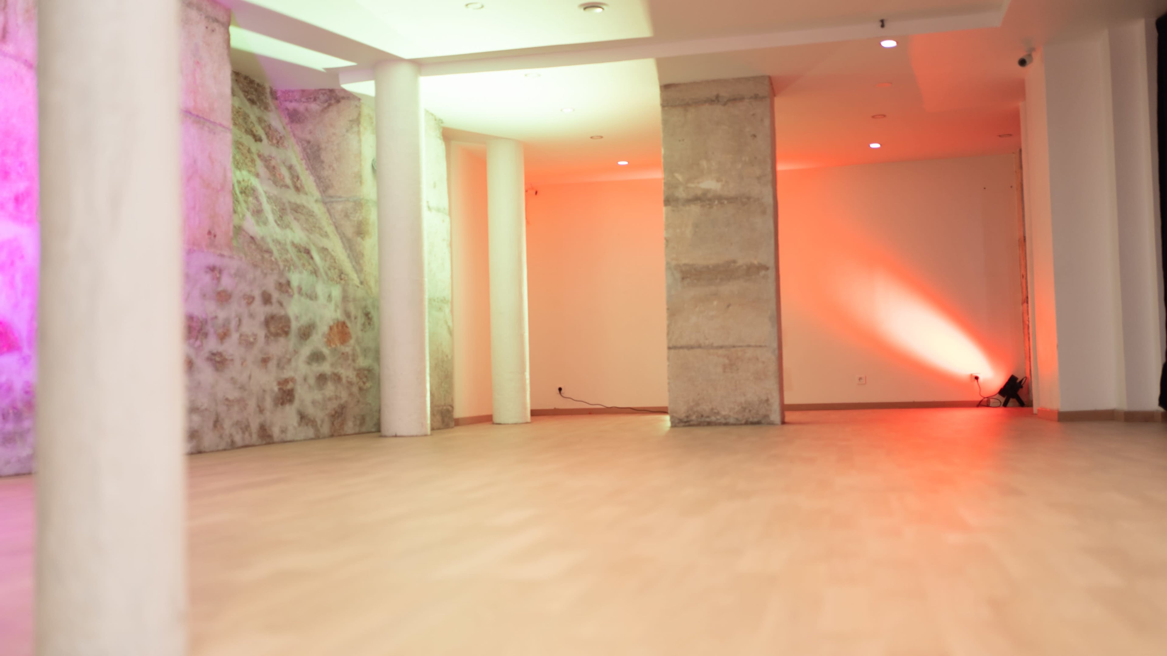 An empty room with stone walls, wooden flooring, and colored lighting coming from the ceiling.