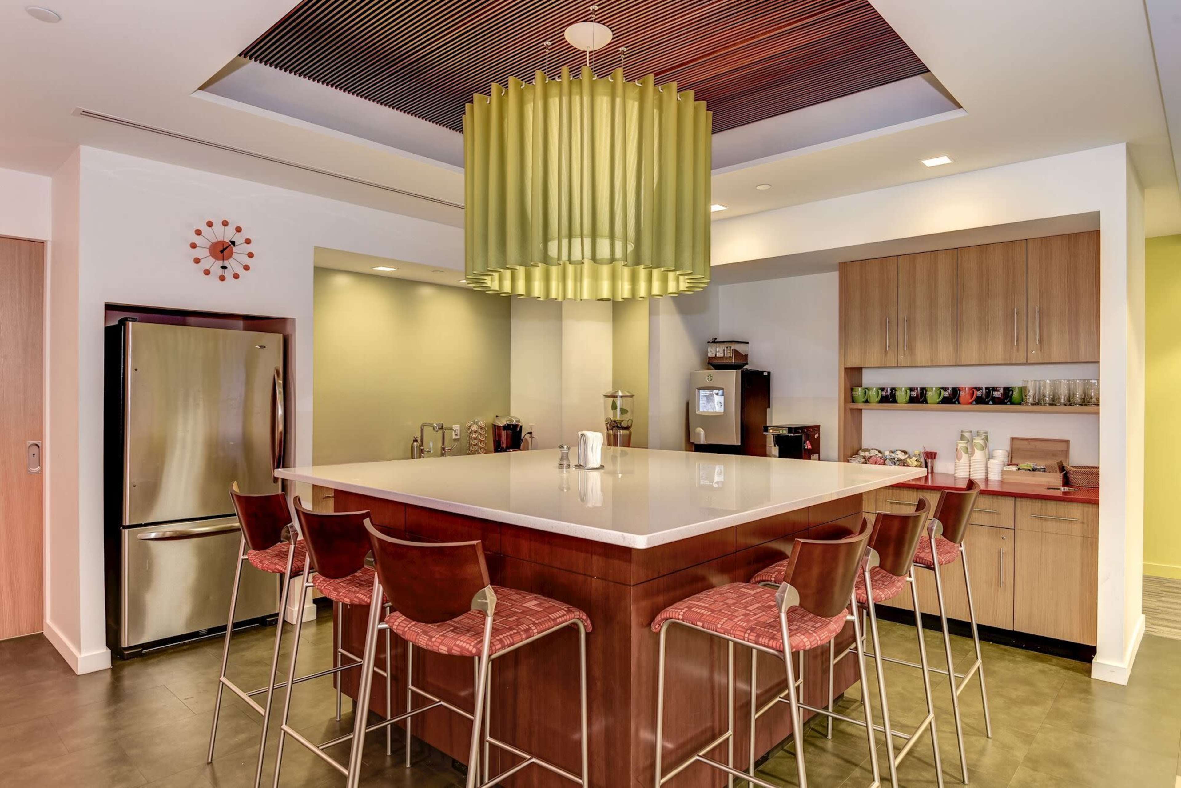 A modern kitchen with a central island, bar stools, stainless steel appliances, and a distinctive green pendant light above.