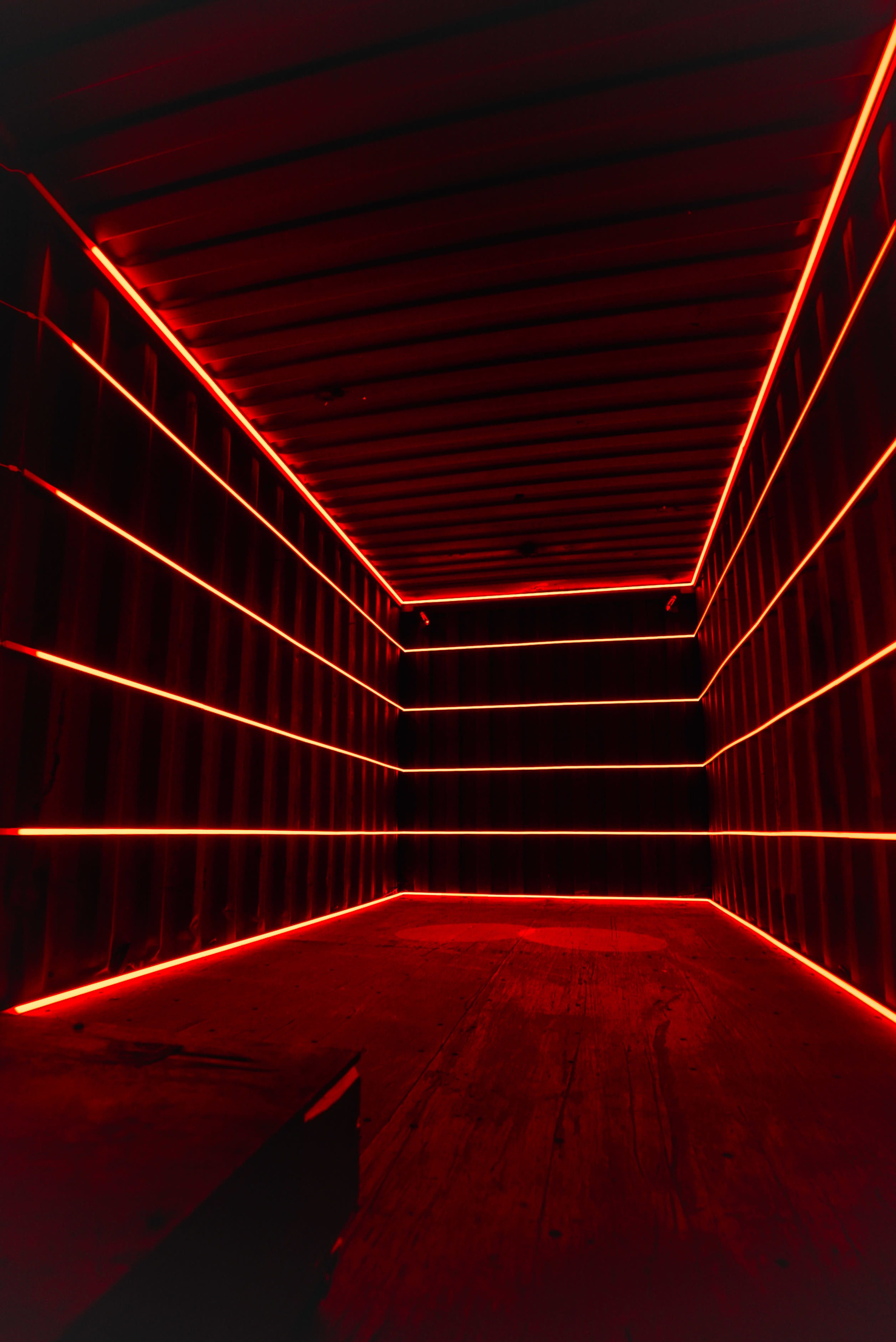 The image shows a dimly lit shipping container illuminated by red LED strips along the walls and ceiling.