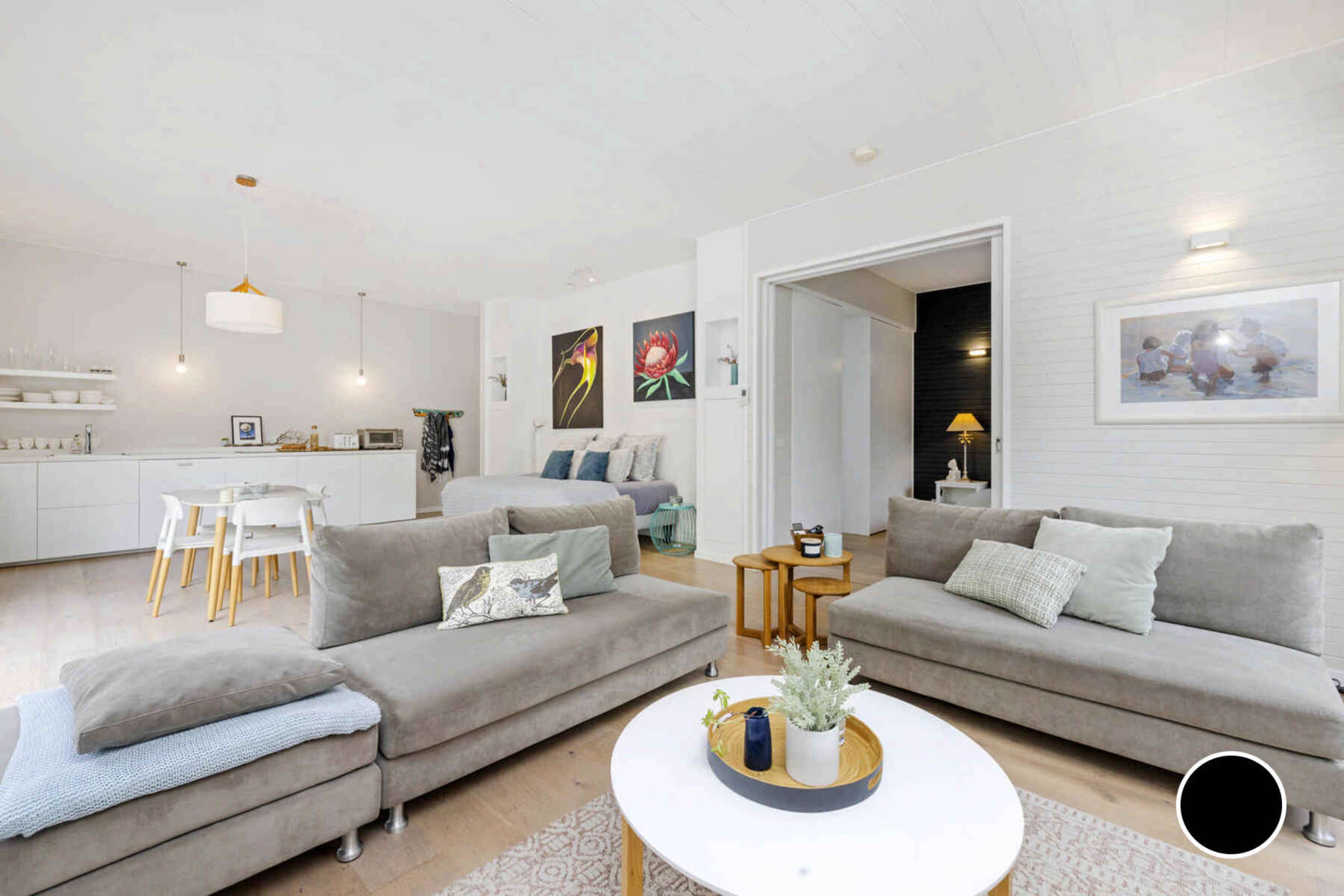 The room features a modern open-concept living space with gray sofas, a circular coffee table, and a dining area with white furniture.