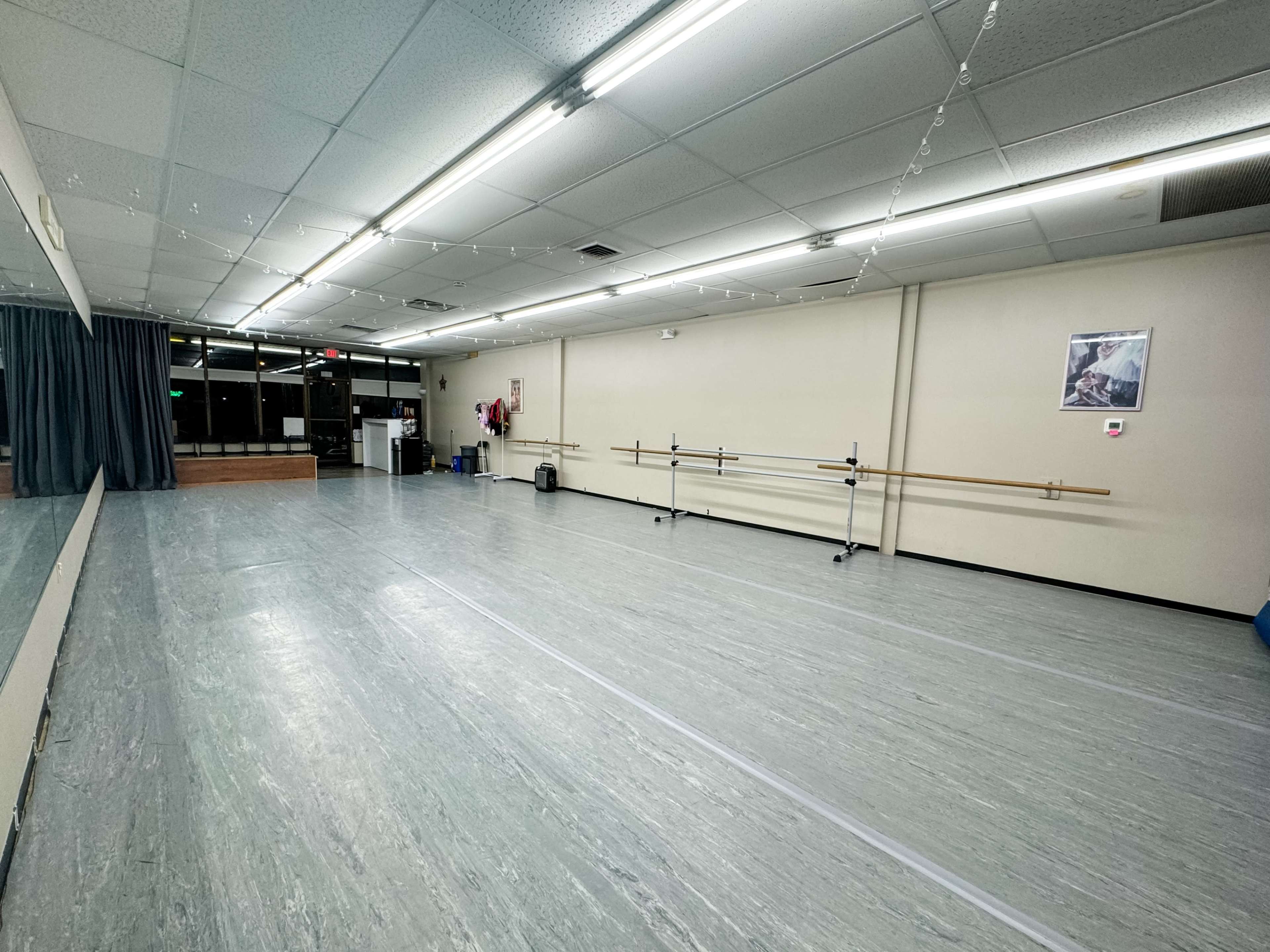 The image shows an empty dance studio with a wooden ballet barre along one wall and mirrors reflecting the space.