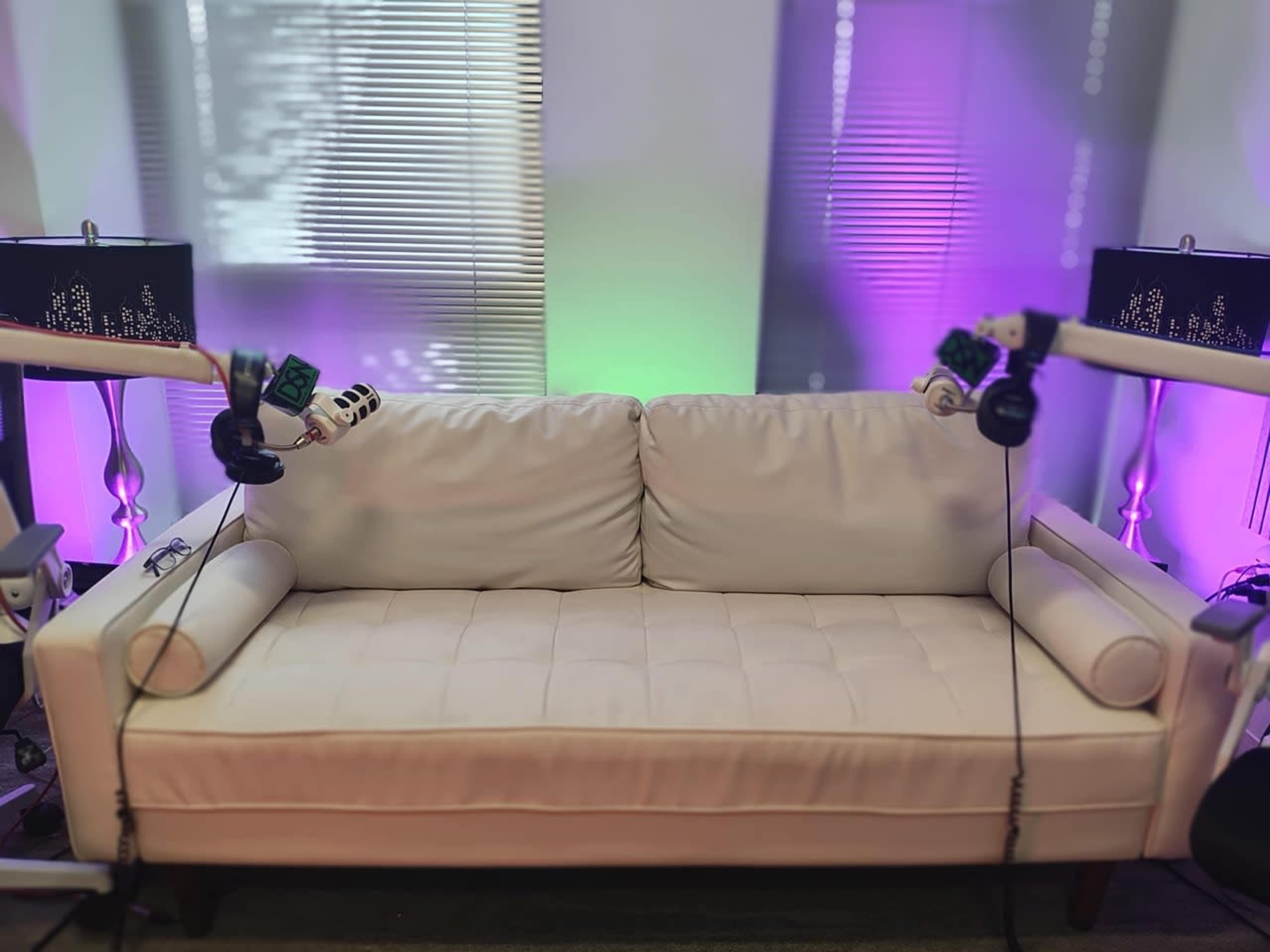 The image shows a light-colored couch positioned between two lamp stands with decorative lamps, under soft purple and green lighting.