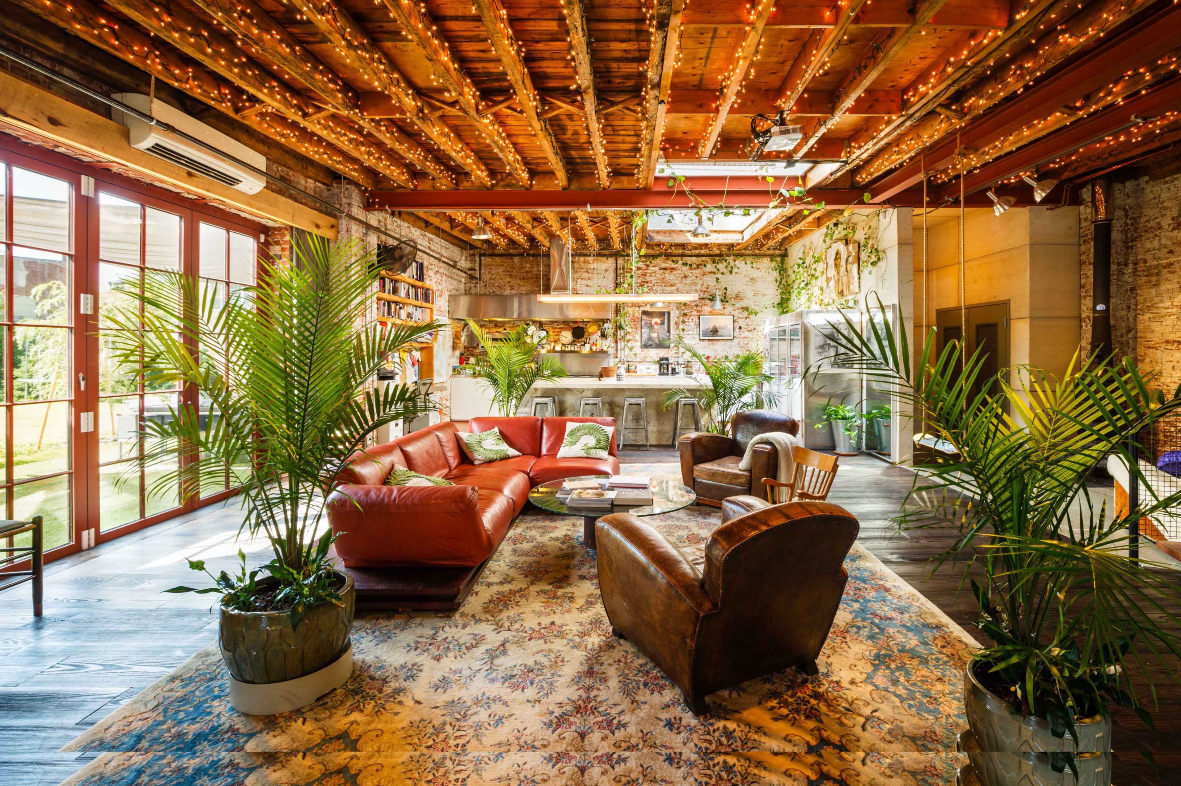 A spacious, modern living room features leather sofas, potted plants, and rustic decor with exposed wooden beams and a vibrant area rug.