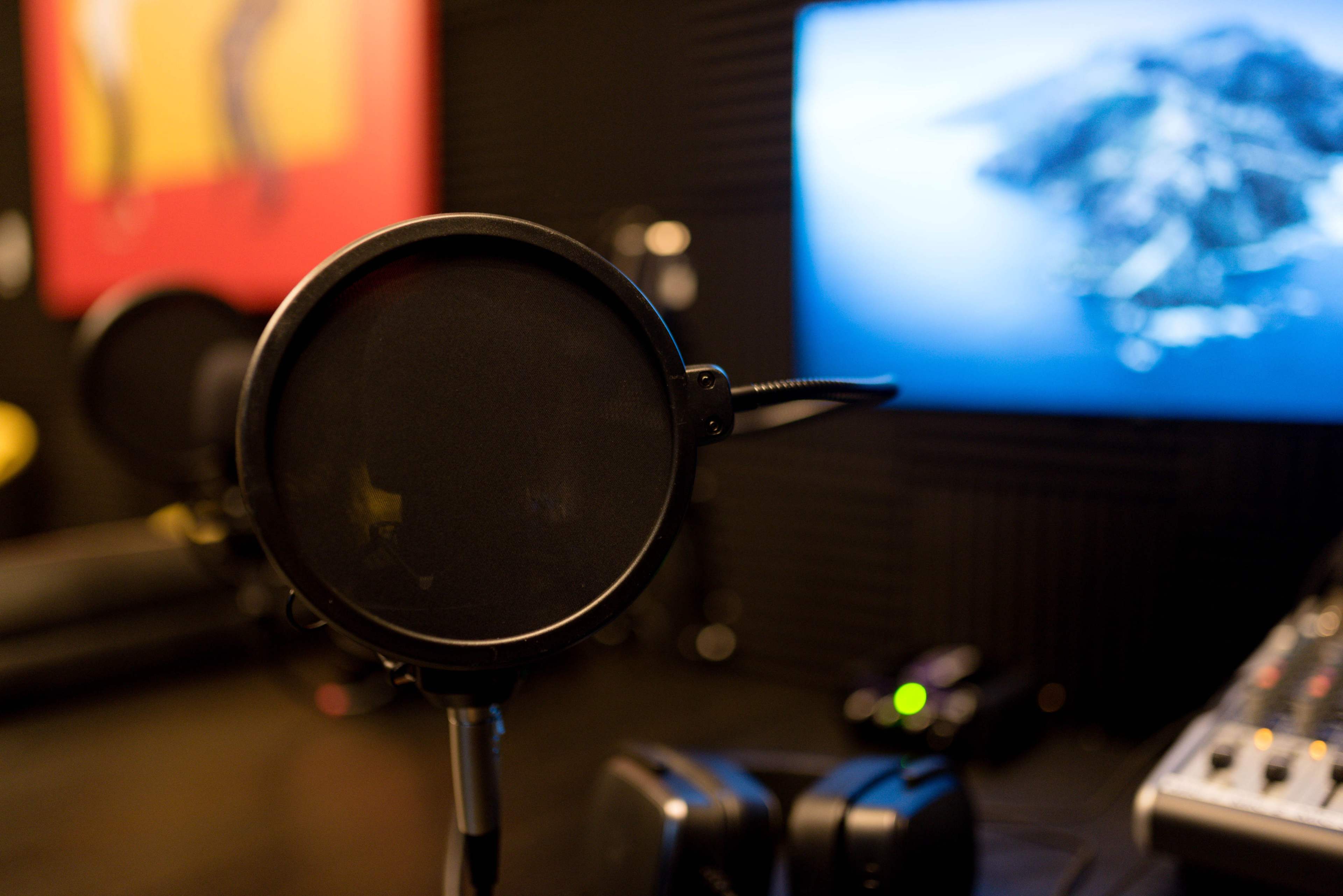 A black pop filter is positioned in front of a microphone in a recording studio, with a computer display showing an island in the background.
