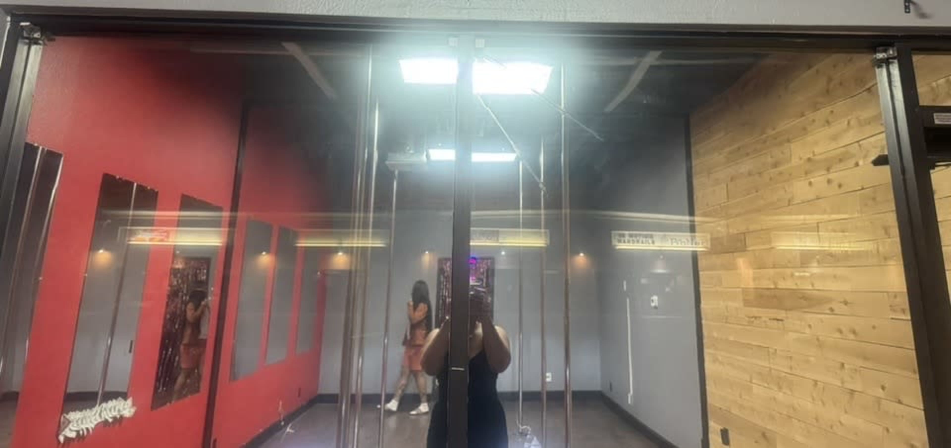 The image shows a glass door reflecting a brightly lit room with red and wooden walls, where a person is partially visible.