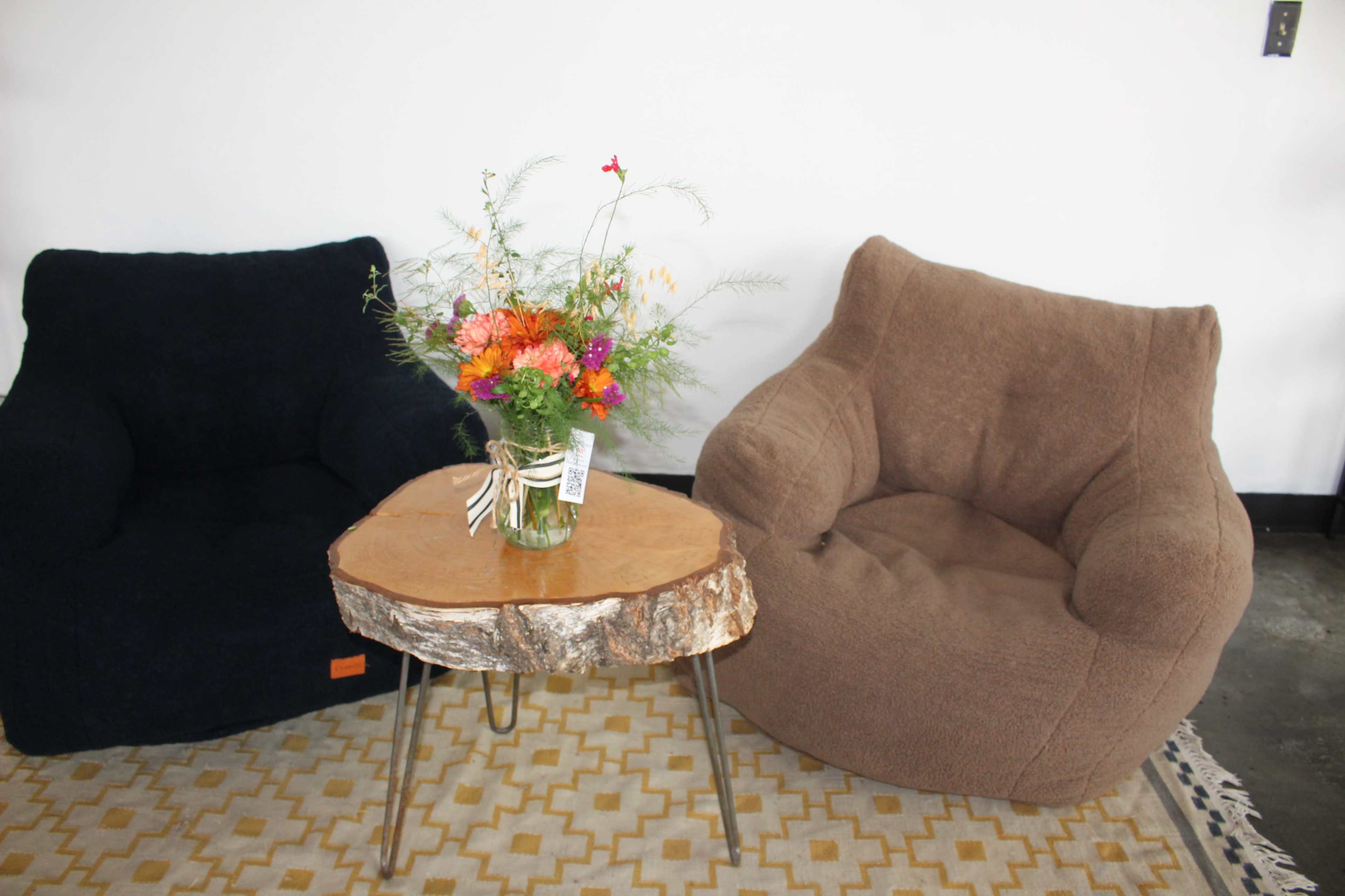 Two armchairs in dark blue and light brown are positioned on a patterned rug, with a wooden table featuring a floral arrangement in the center.