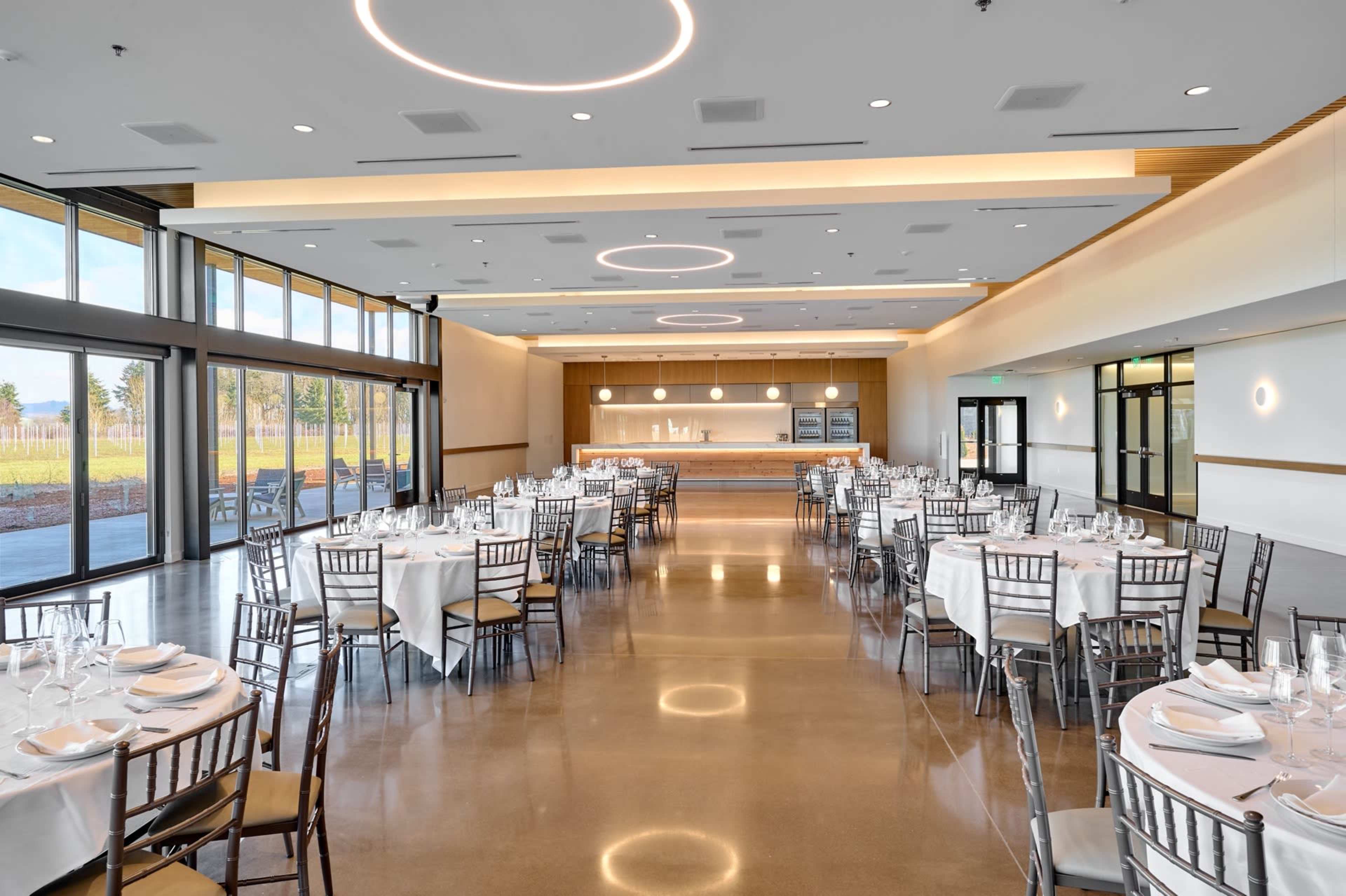 A spacious dining hall features neatly arranged tables with white tablecloths and a modern bar area in the background.