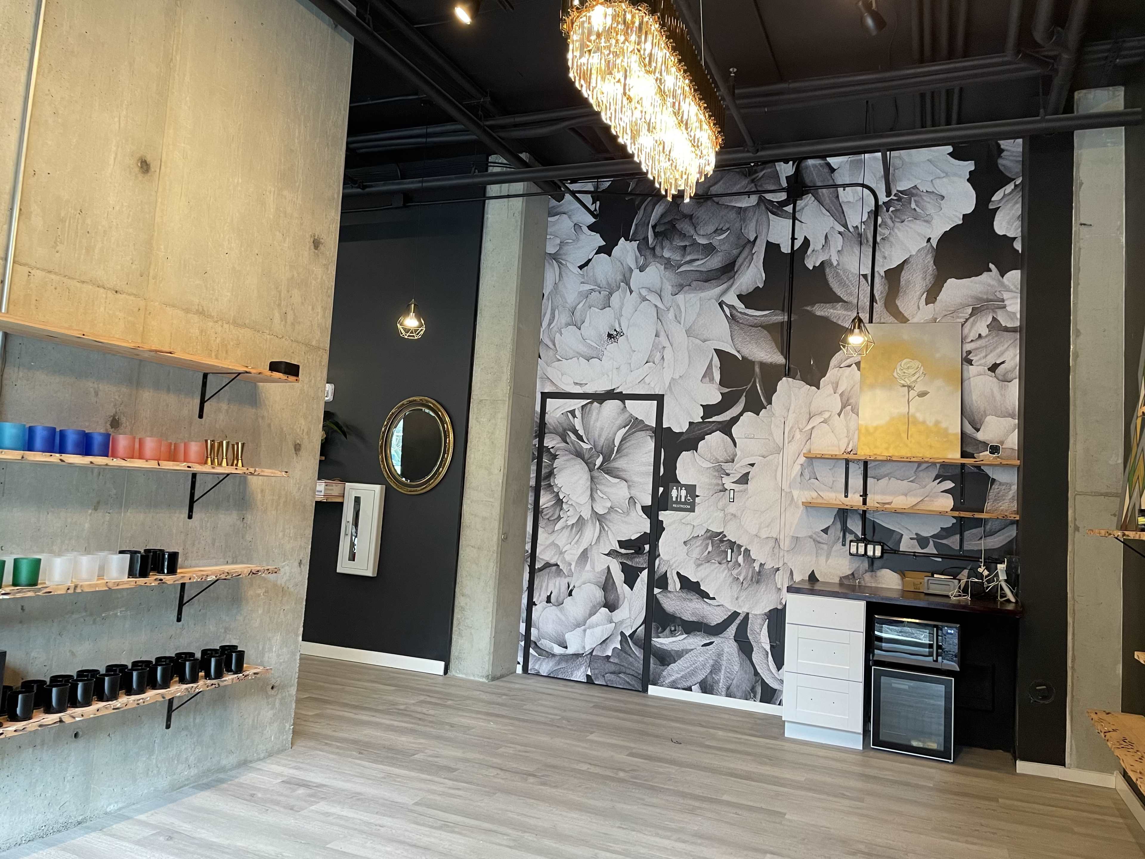 A modern interior space featuring a floral mural, light wood shelves with colored containers, a mirrored wall decor, and a small kitchenette area in the corner.