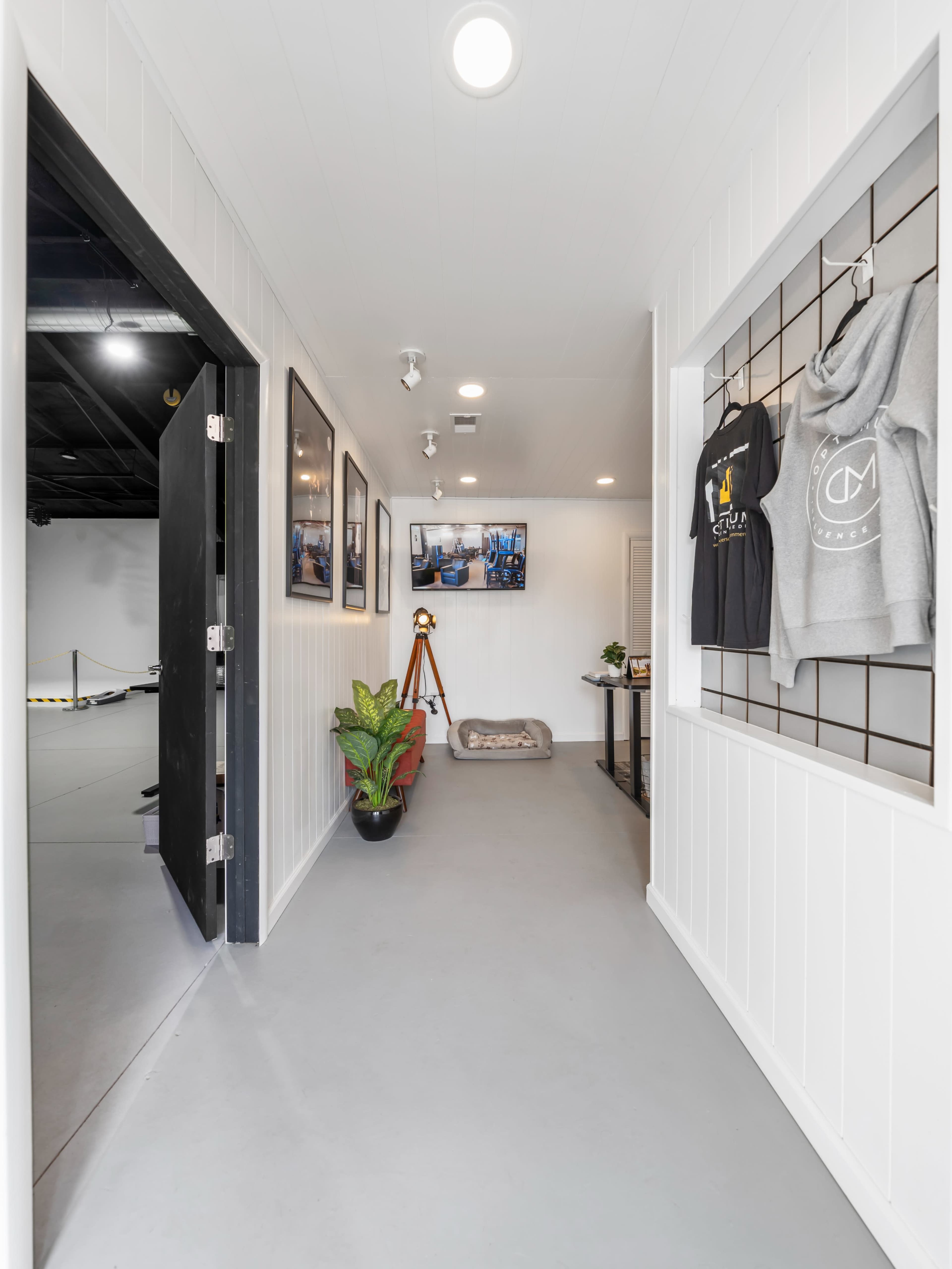 A narrow hallway leading to a bright, minimalist space featuring clothing displays, artwork on the walls, and a small seating area.