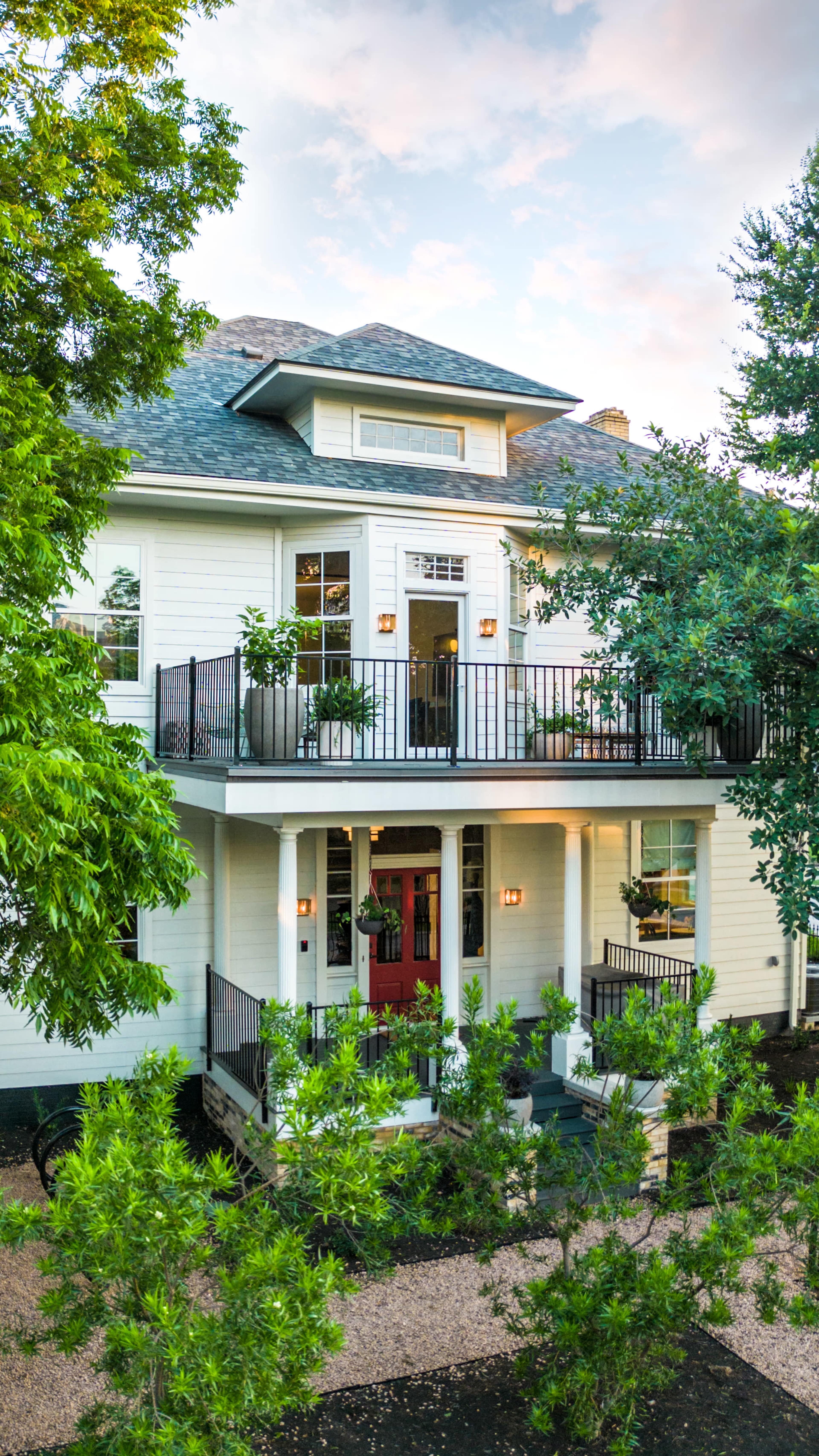 The image shows a two-story white house with a covered porch, black railings, and green landscaping.