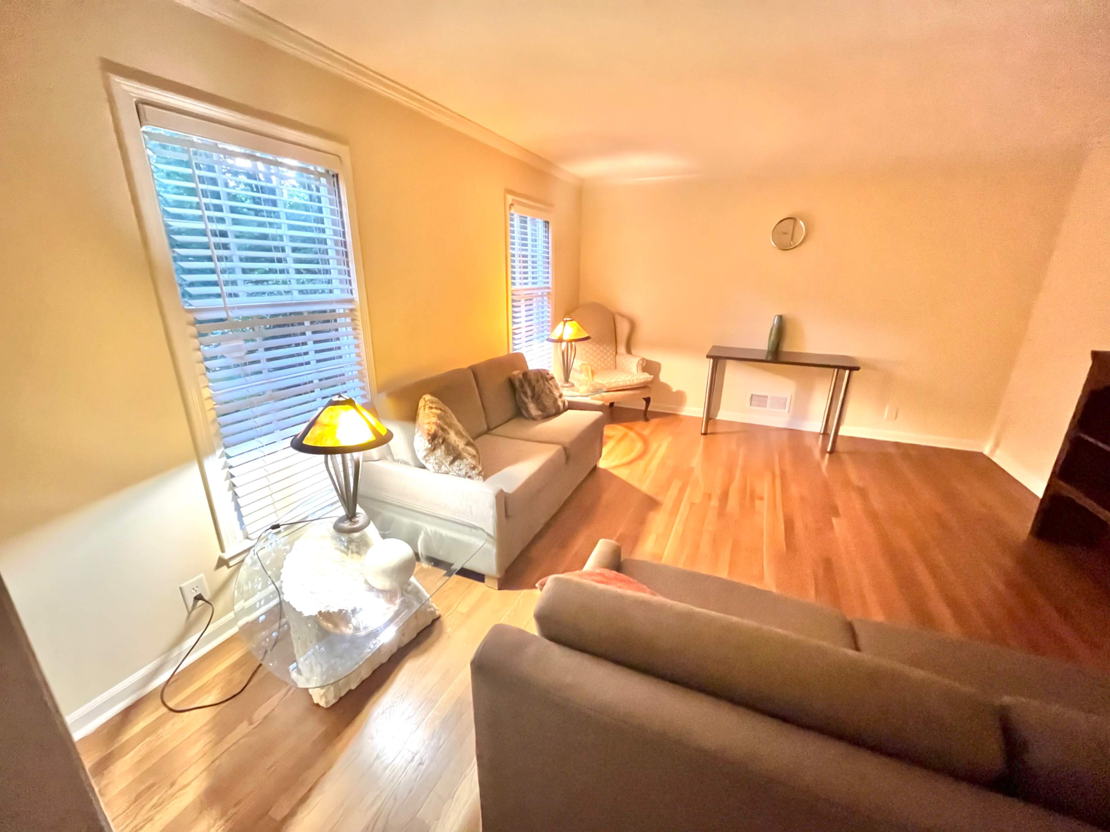 The image shows a living room with two sofas, two lamps, and large windows letting in natural light.