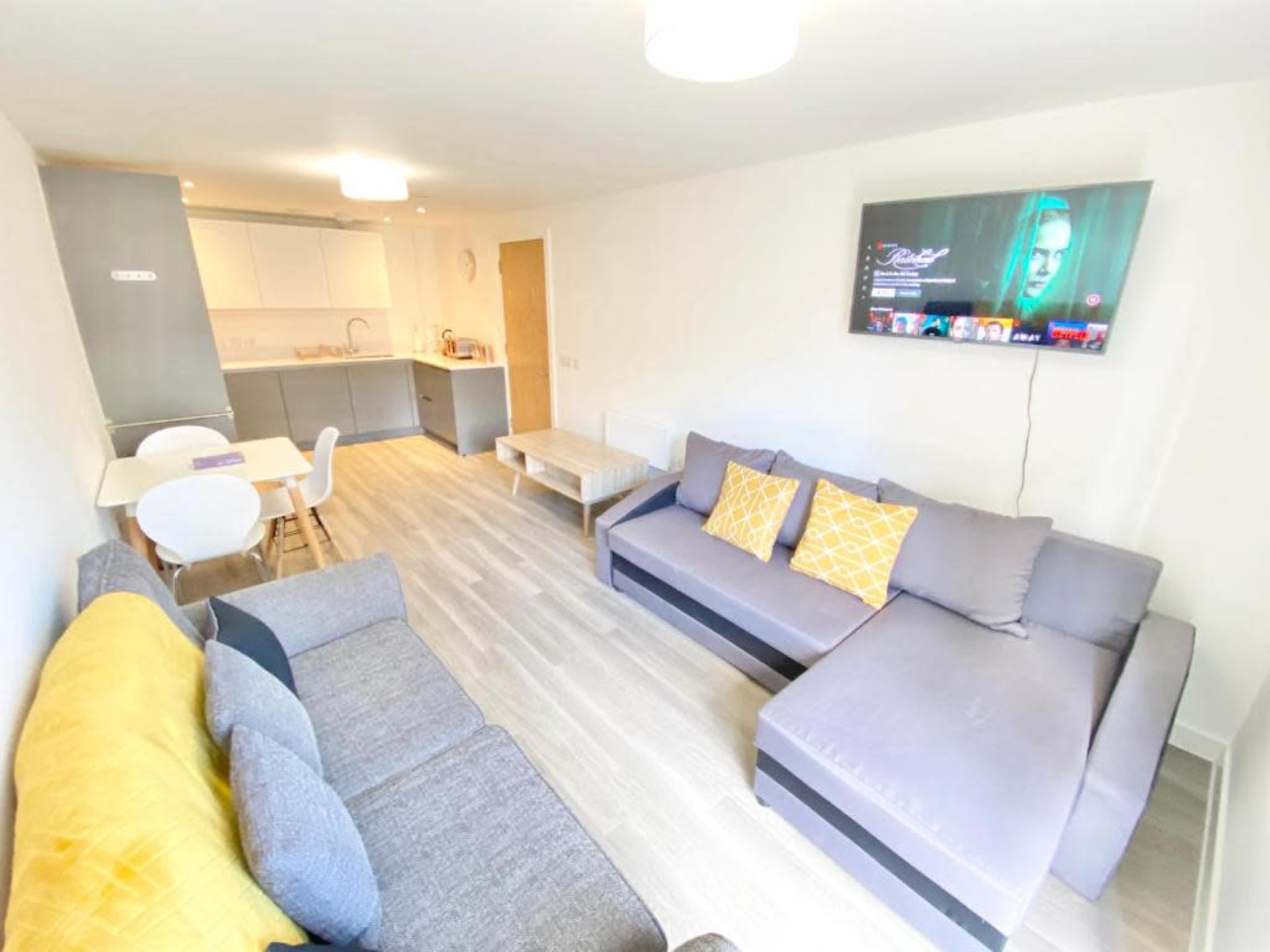 A modern living room with gray couches, a light-colored table, and a wall-mounted television.