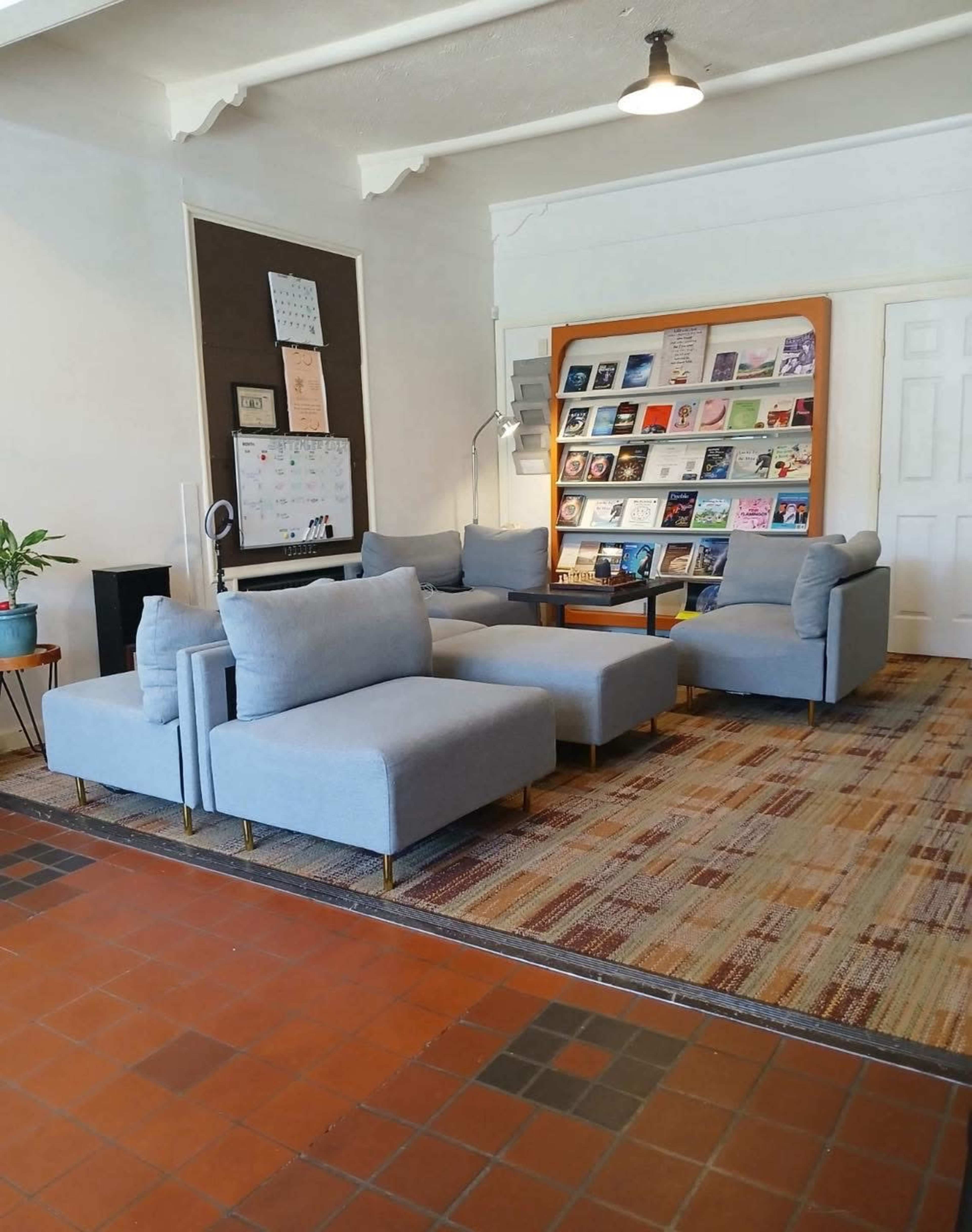 The image shows a cozy seating area with blue armchairs and a couch, alongside a book display on a wooden shelf against a light wall.