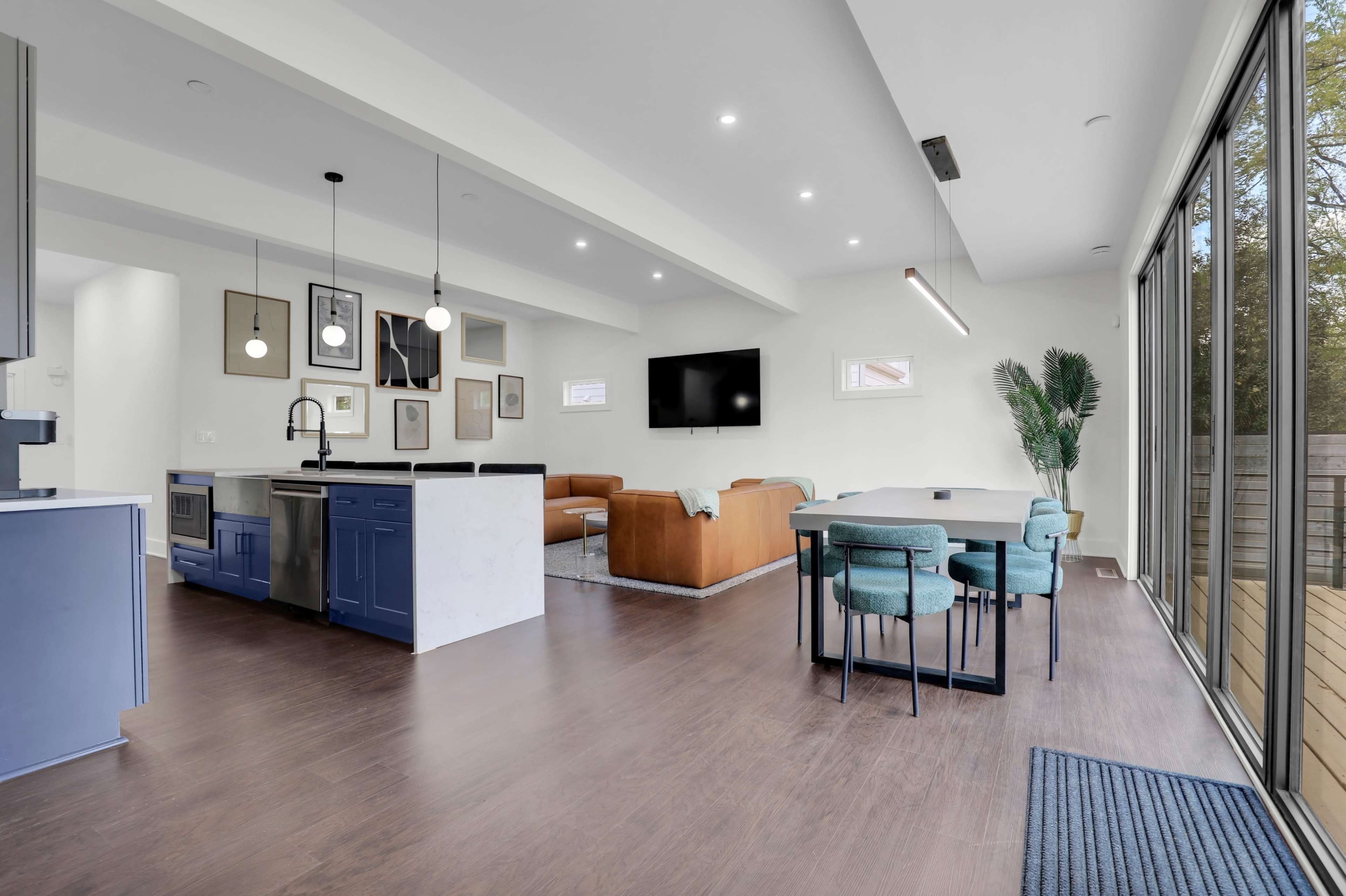 The image shows a modern open-concept living space featuring a kitchen, dining area, and lounge with large windows.