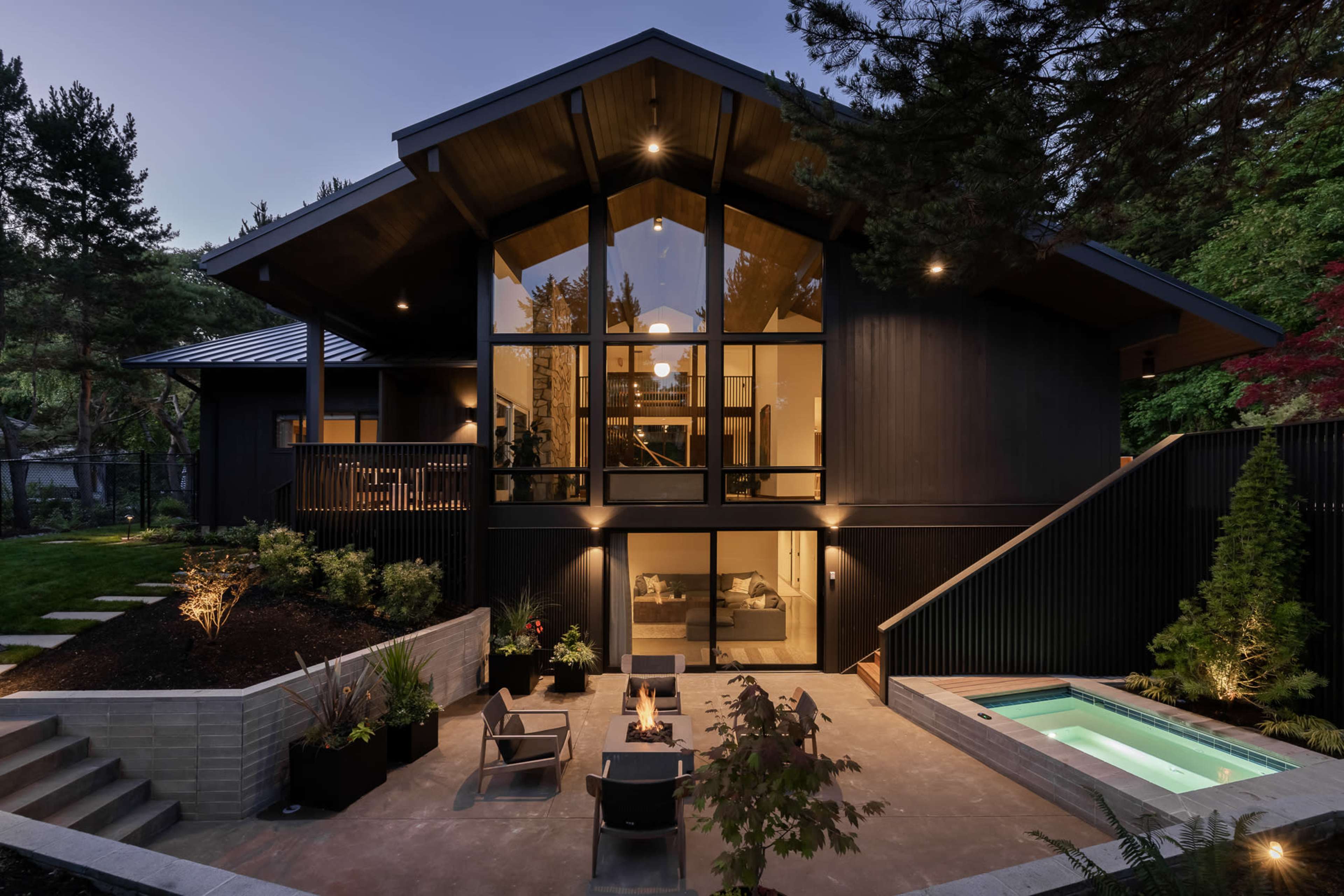 A modern house with large glass windows, a landscaped yard, a small swimming pool, and a fire pit in the outdoor seating area.