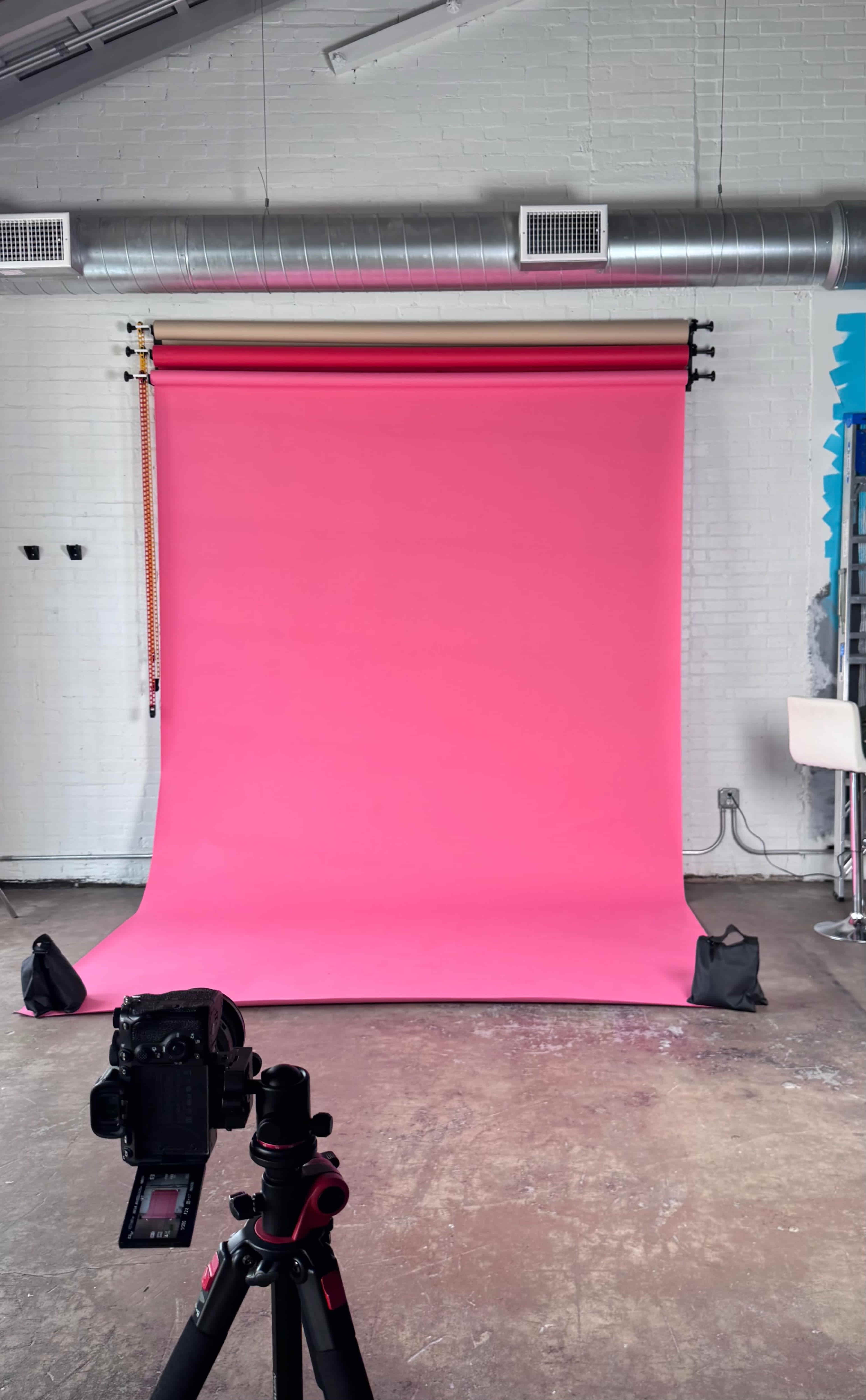 A bright pink backdrop is set up in a photography studio with a camera positioned in front of it.