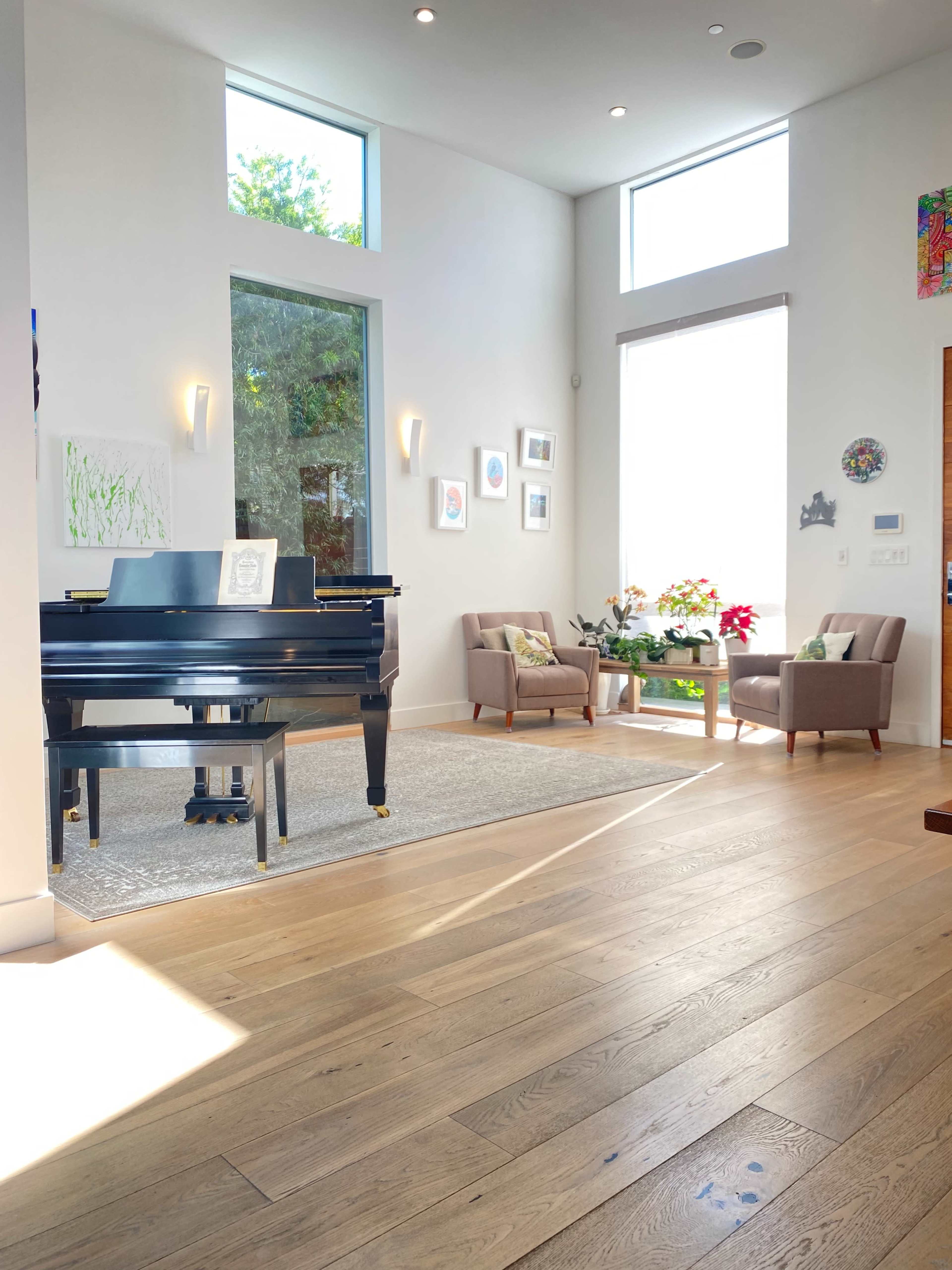 A well-lit modern living room with a black piano, two armchairs, and decorative artwork on the walls.