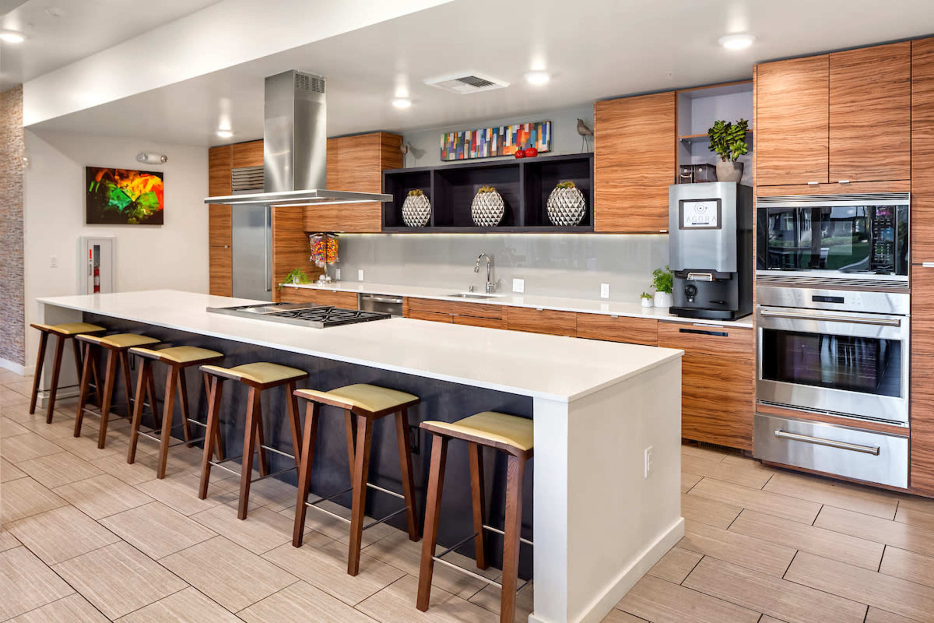 A modern kitchen featuring a long island with barstools, wooden cabinets, stainless steel appliances, and a minimalist design.