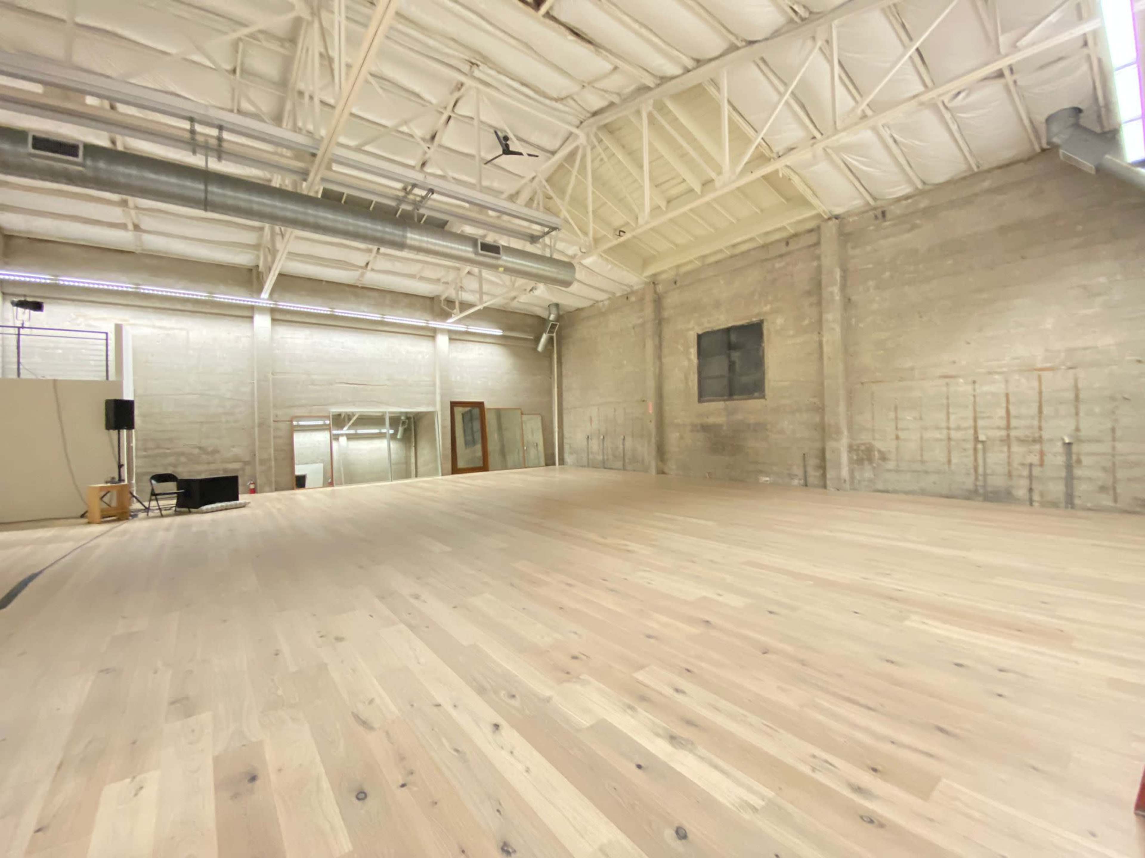 A spacious studio with wooden flooring, high ceilings, and a few large mirrors mounted on the walls.