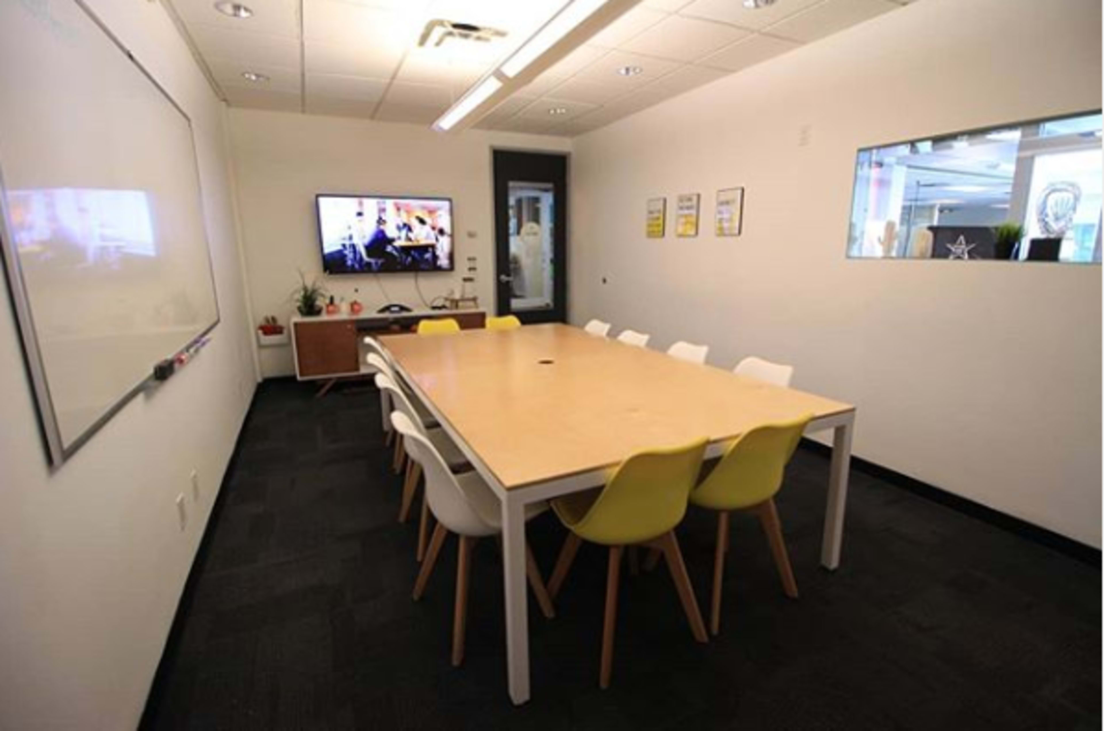 A conference room features a long table surrounded by chairs, a television on the wall, and a whiteboard.