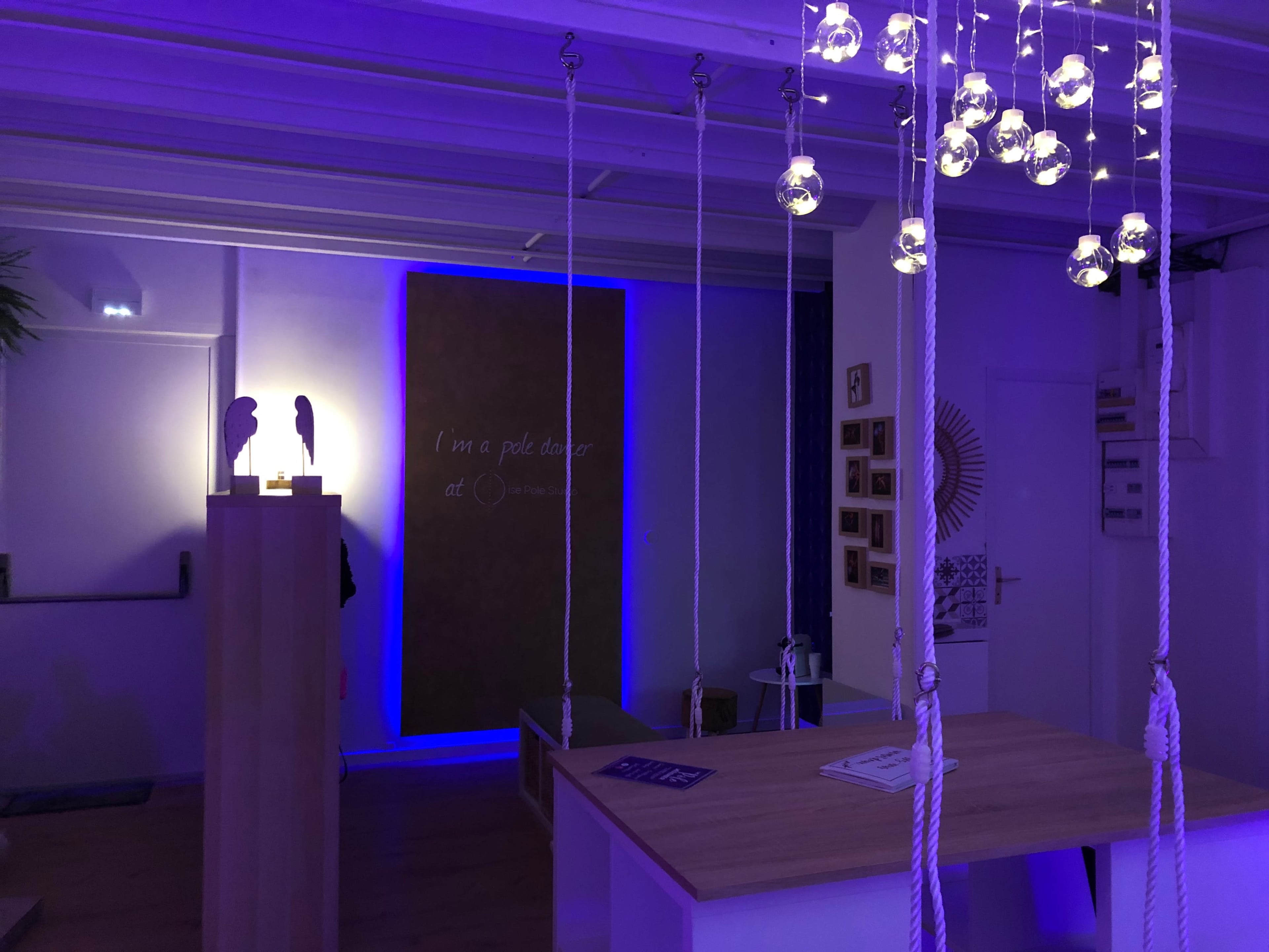 The interior of a modern room features a wooden table, rope swings, and blue ambient lighting highlighting a wall with text.