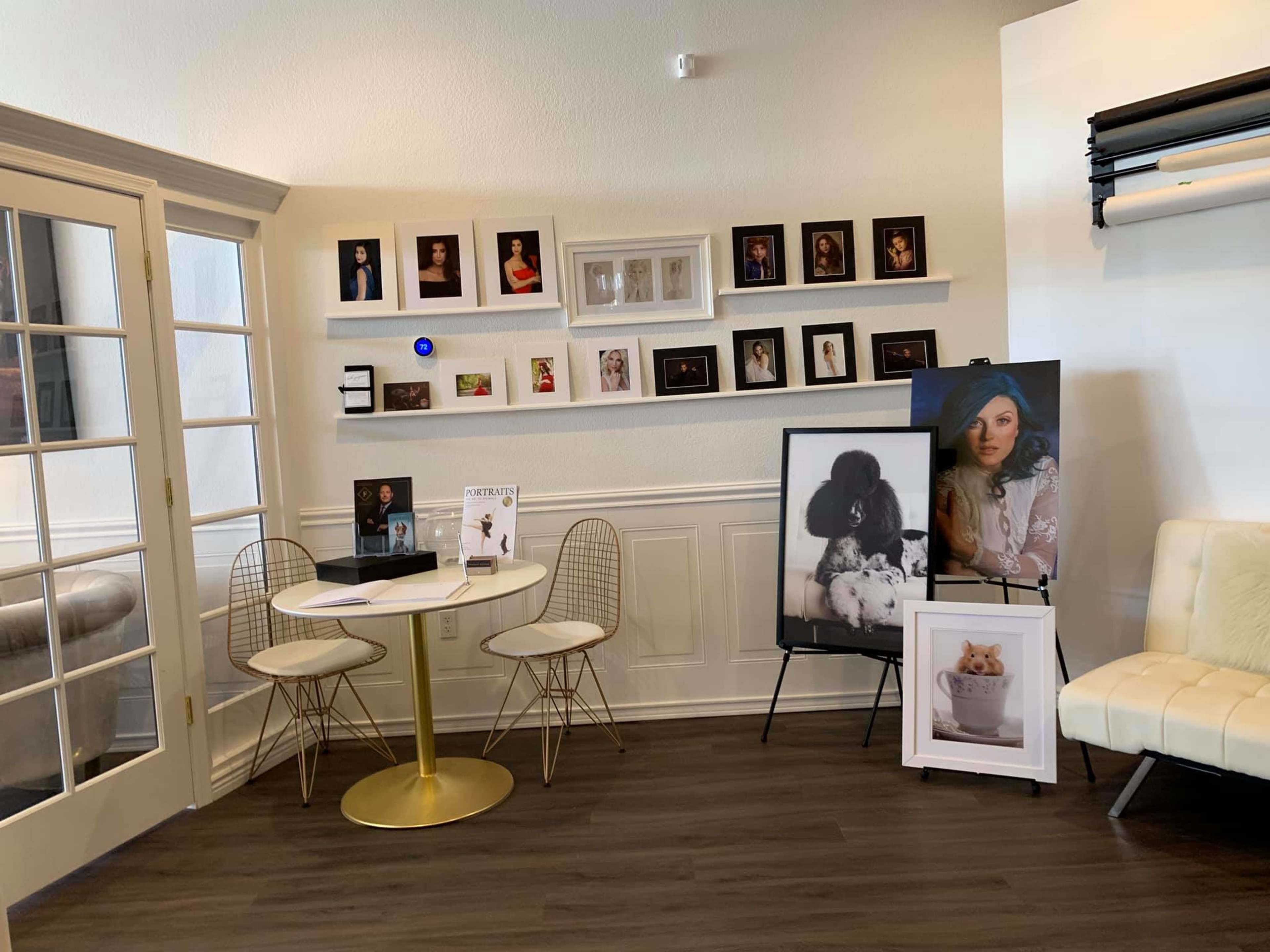 A modern interior space with a round gold table and two wire chairs, featuring framed photographs on the wall and display stands with promotional materials.