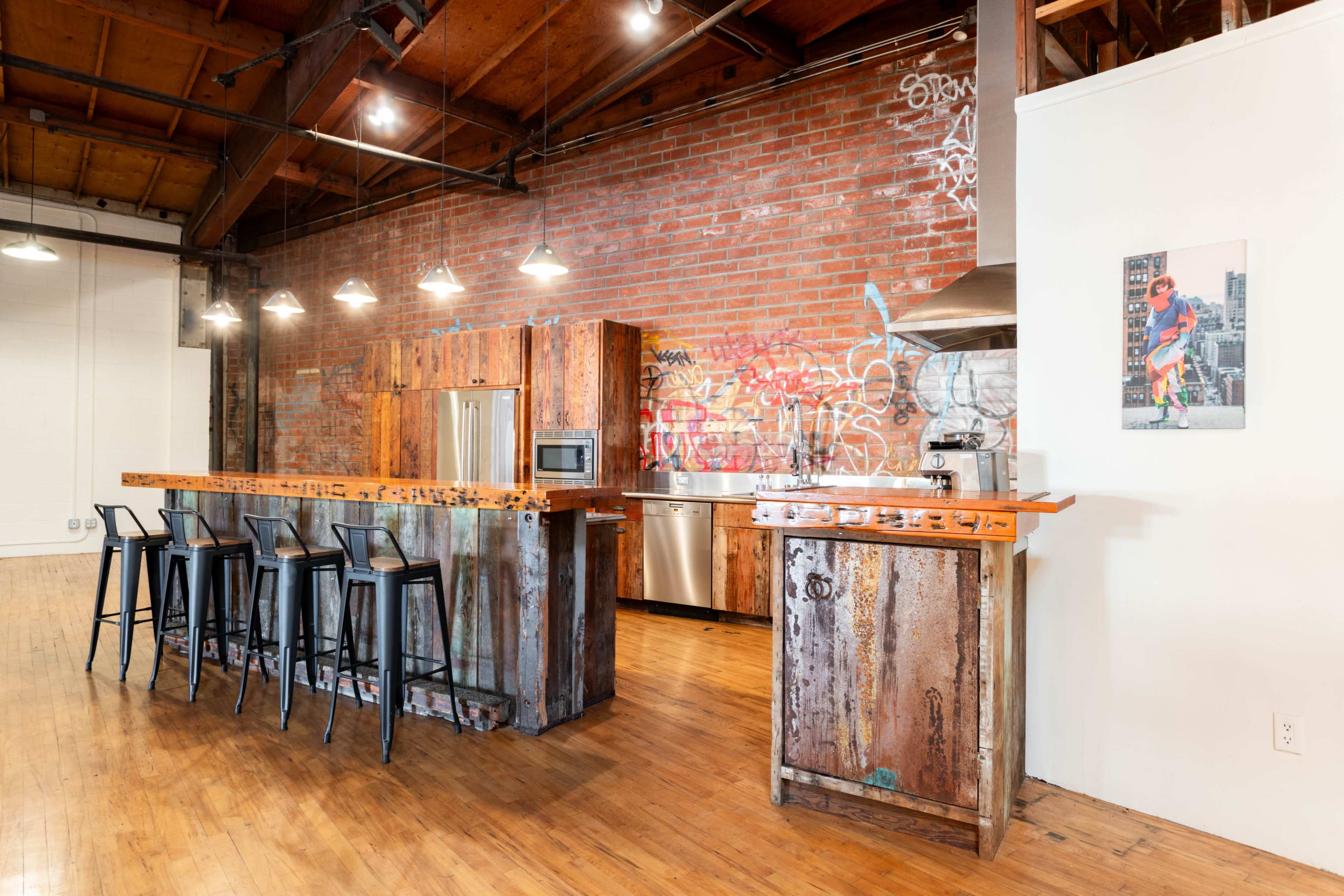 The image shows a modern kitchen with a rustic wooden island, stainless steel appliances, and exposed brick walls adorned with graffiti.